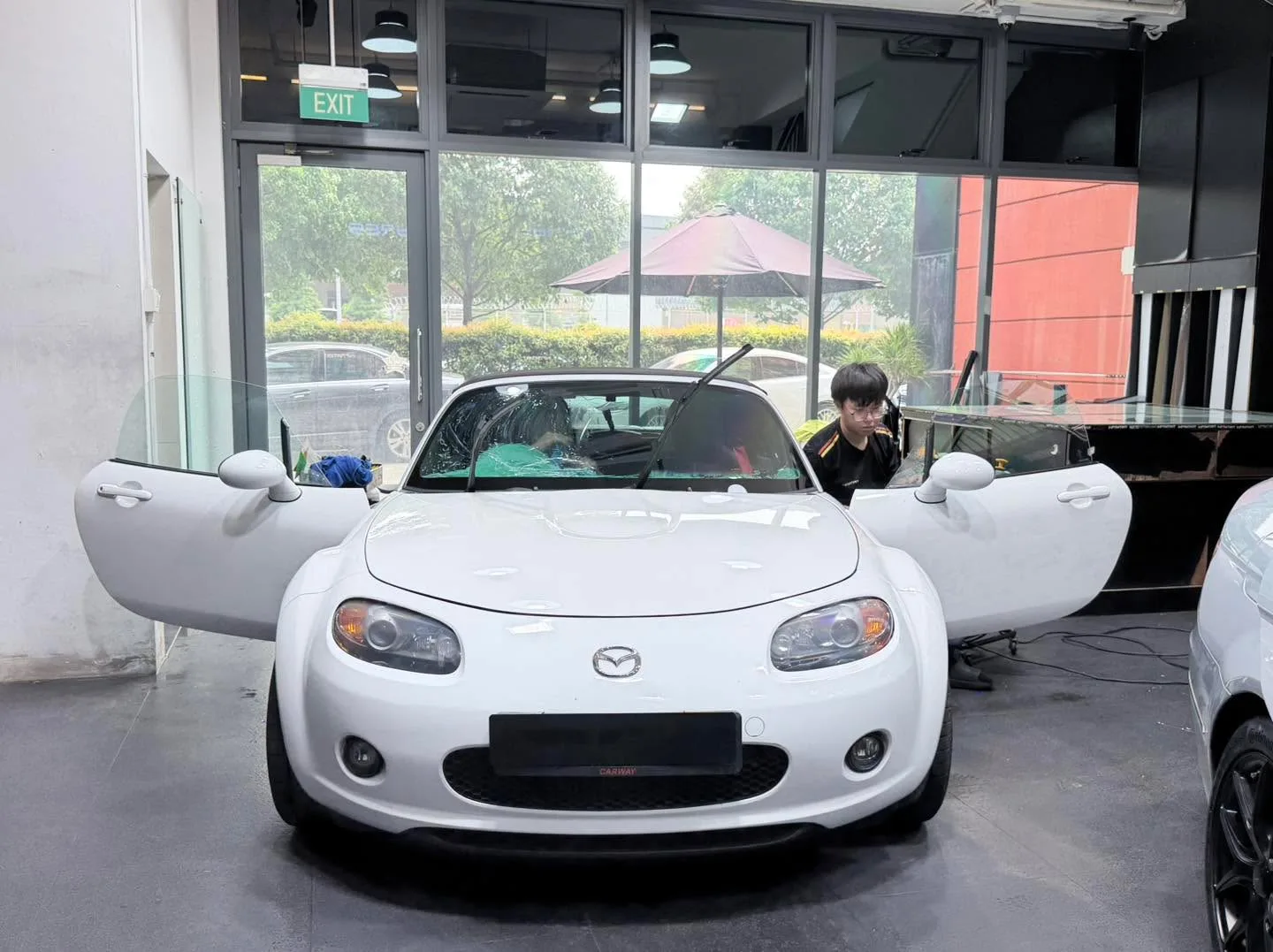 A white Mazda MX-5 convertible with both doors open in the workshop.