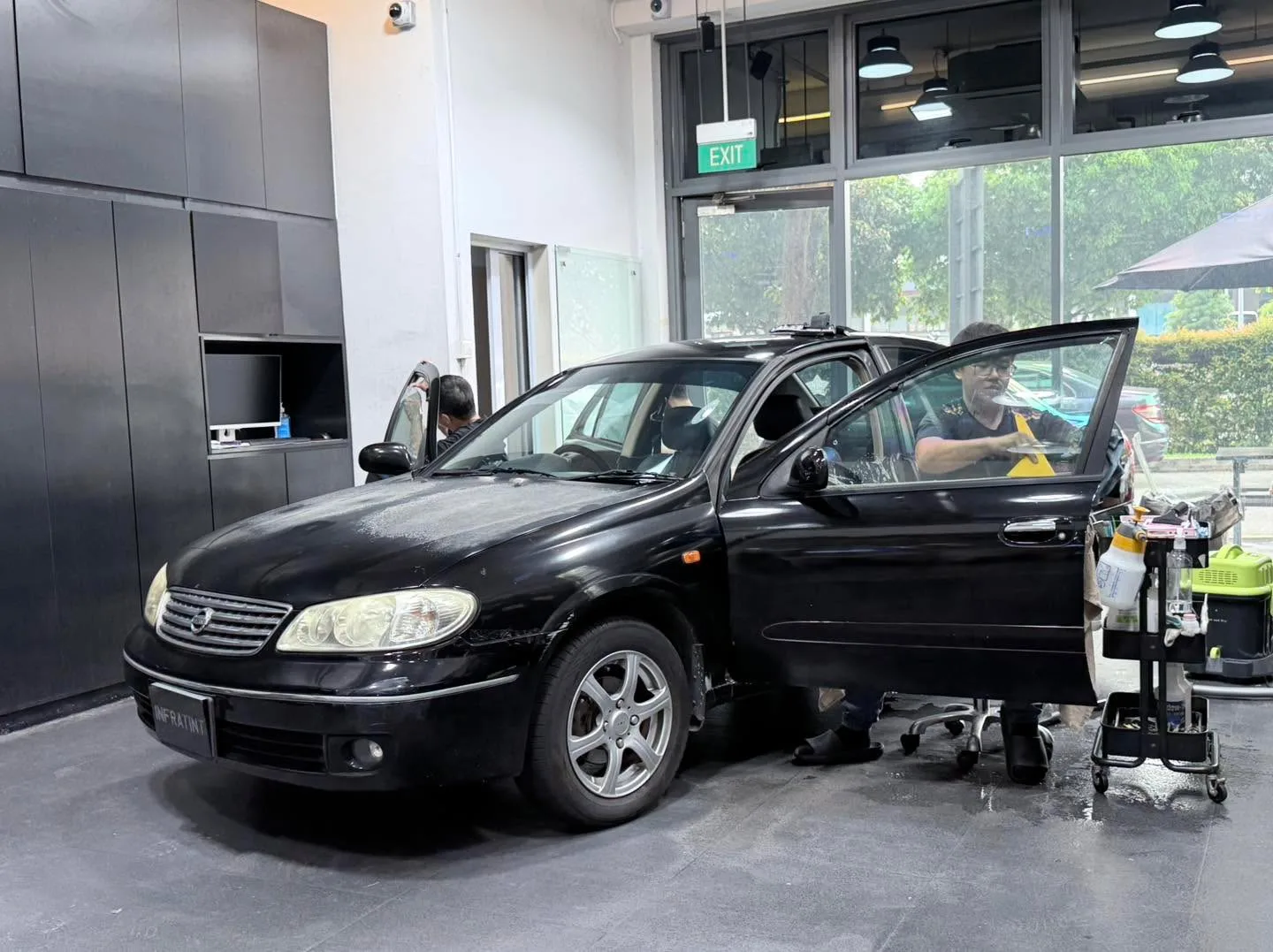 A black Nissan Sunny sedan with rear passenger door open in the workshop.