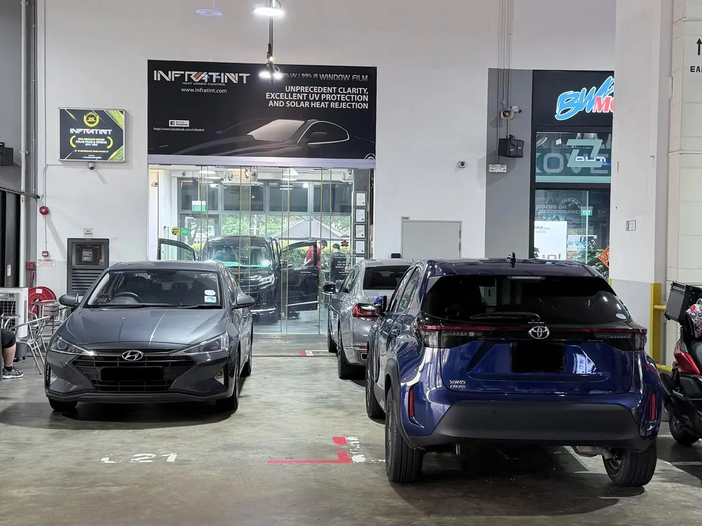 A grey Hyundai and a blue Toyota parked at the workshop entrance in daylight.