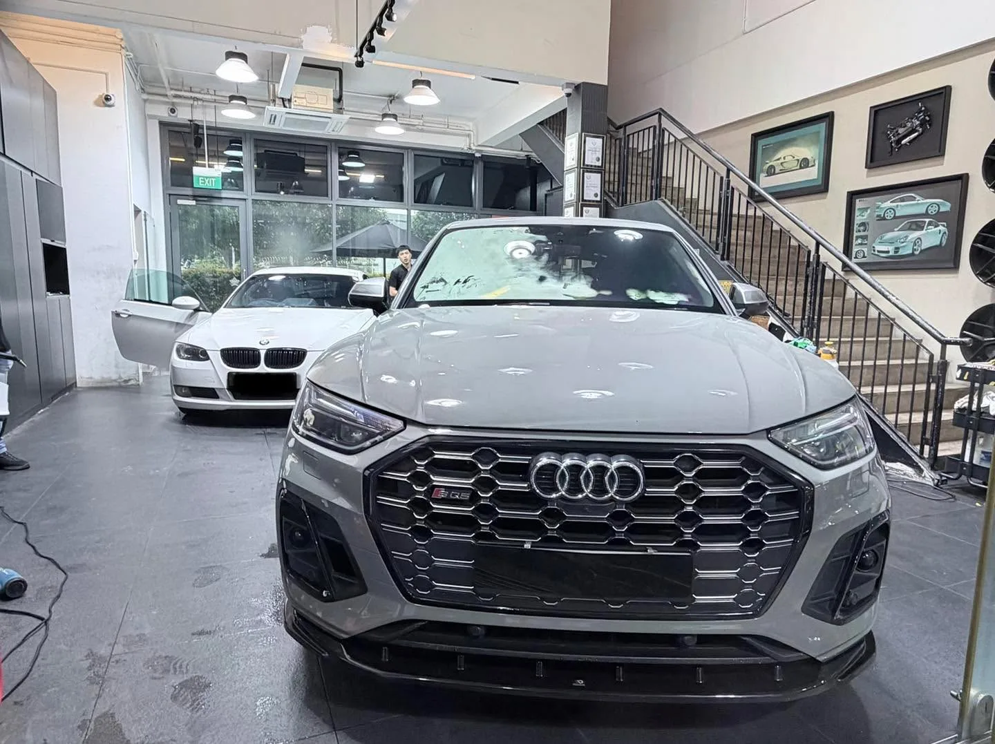 A grey Audi SQ5 with distinctive grille, photographed indoors with a BMW in the background.