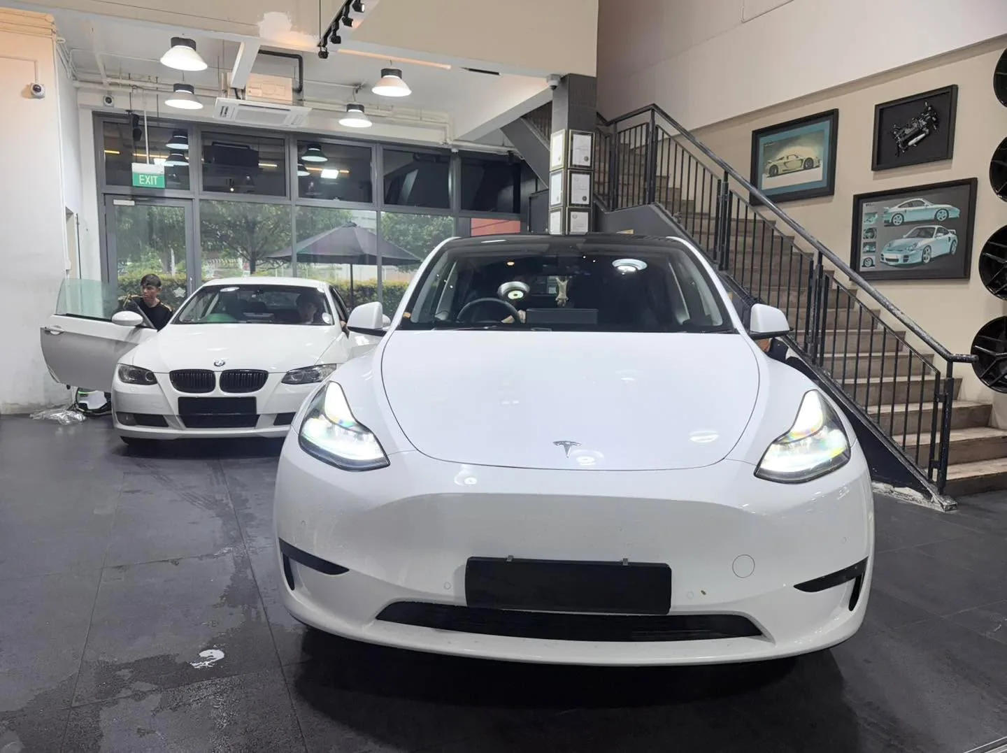 A white Tesla Model Y parked indoors with a white BMW nearby on the left.
