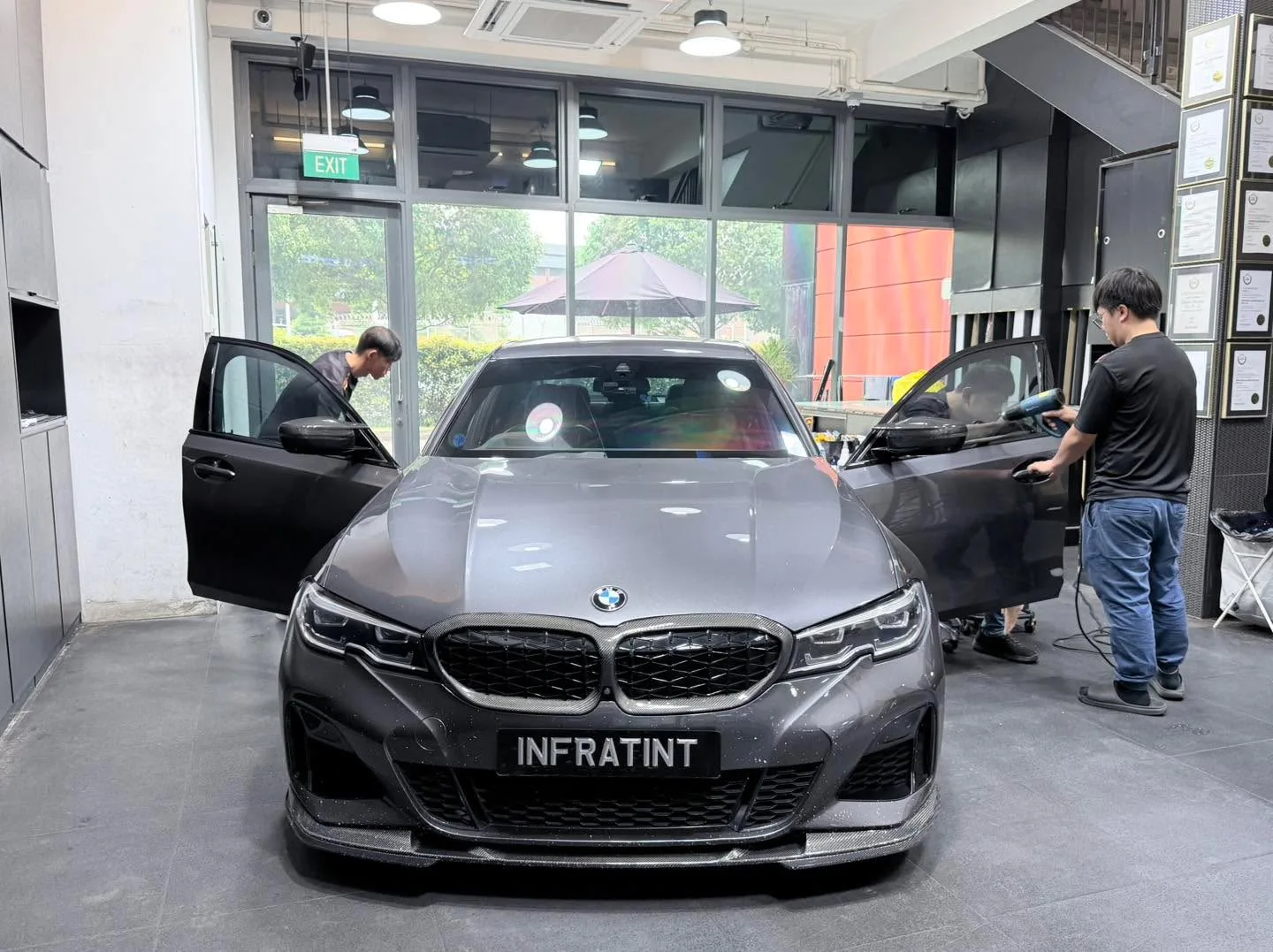 A grey BMW with both doors open as technicians apply window film.