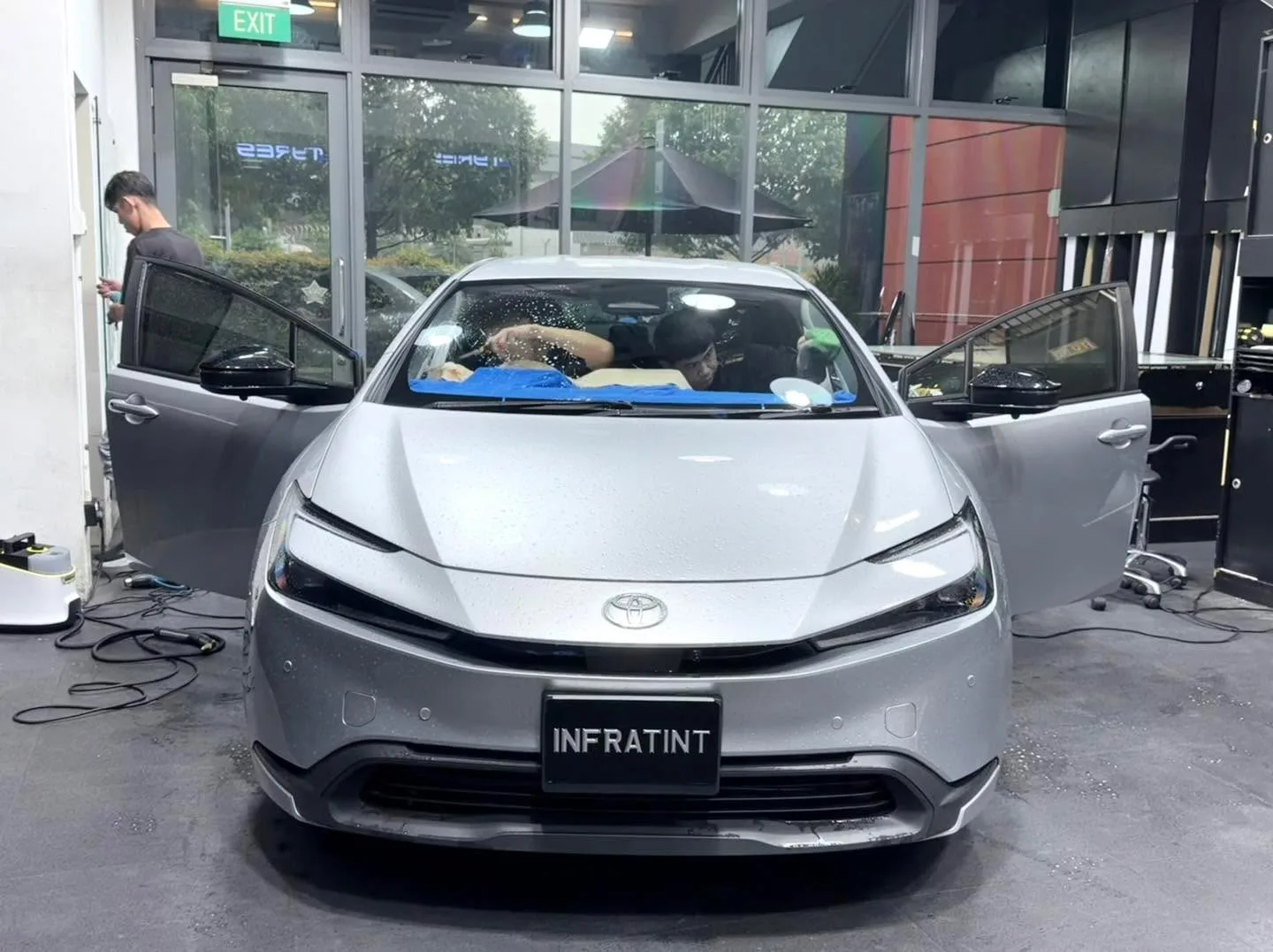 A grey Toyota with open doors and window film being applied by a technician.