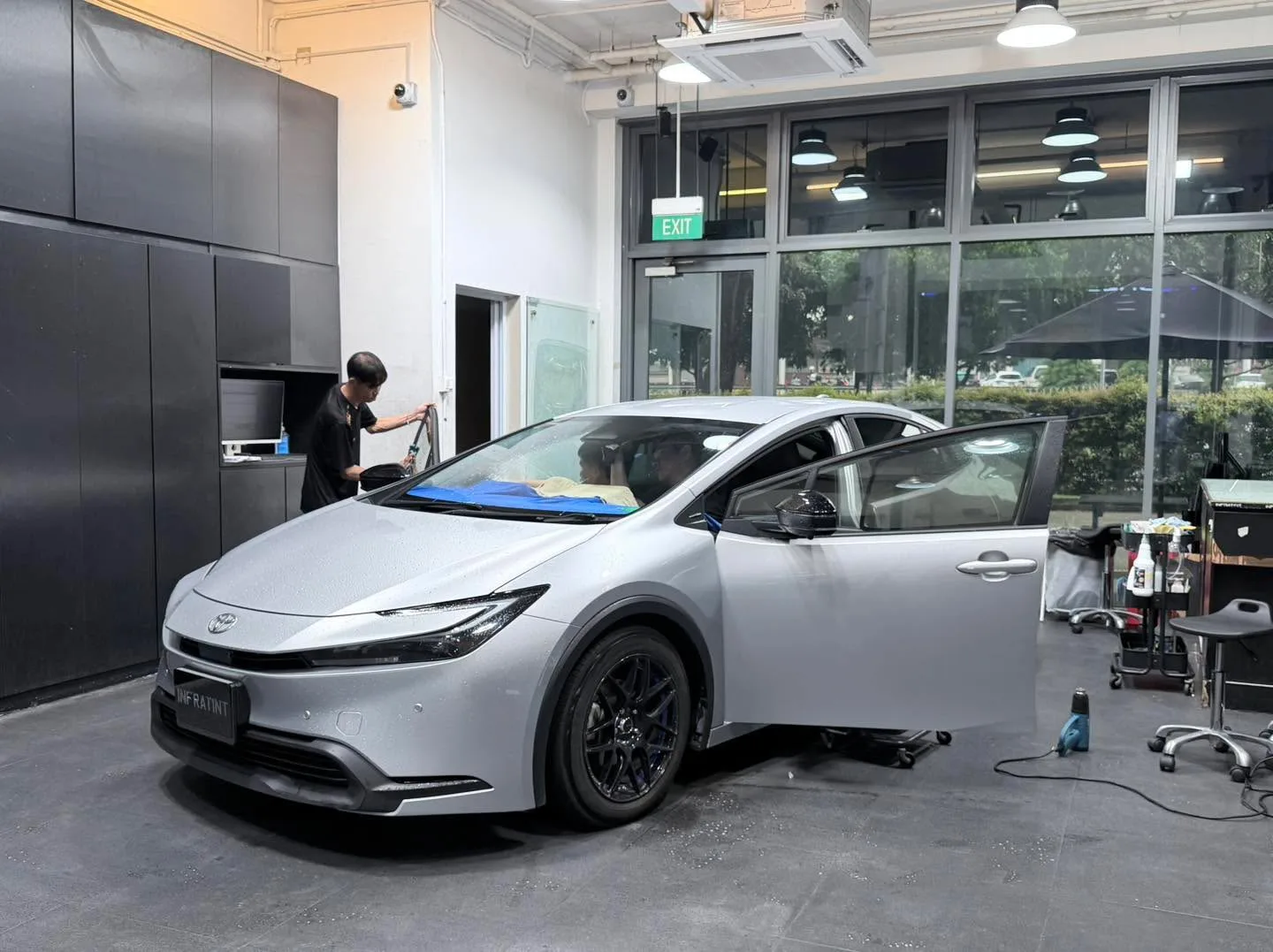 A white Toyota with open doors and blue masking tape visible on the windows during tinting.