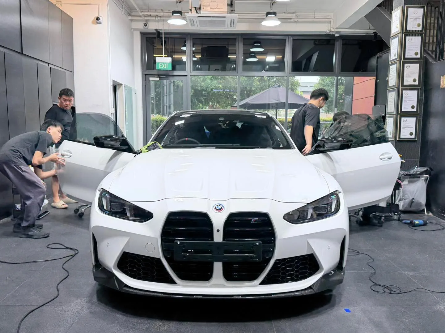 A white BMW sedan with distinctive kidney grille, technicians applying film.