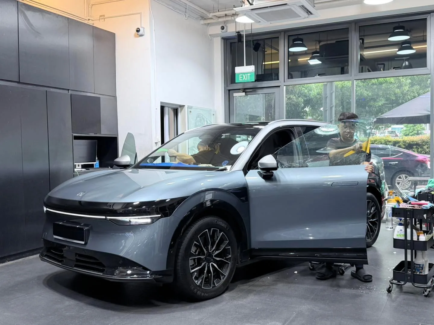 A light grey crossover with open door, technician working on window.