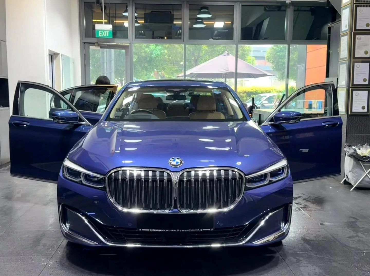 A dark blue BMW 7 Series sedan with doors open, technicians at work.