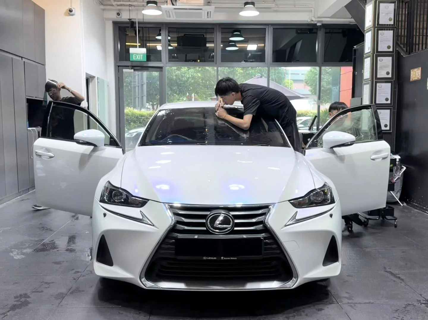 A burgundy Lexus sedan with doors open, technicians applying window film.