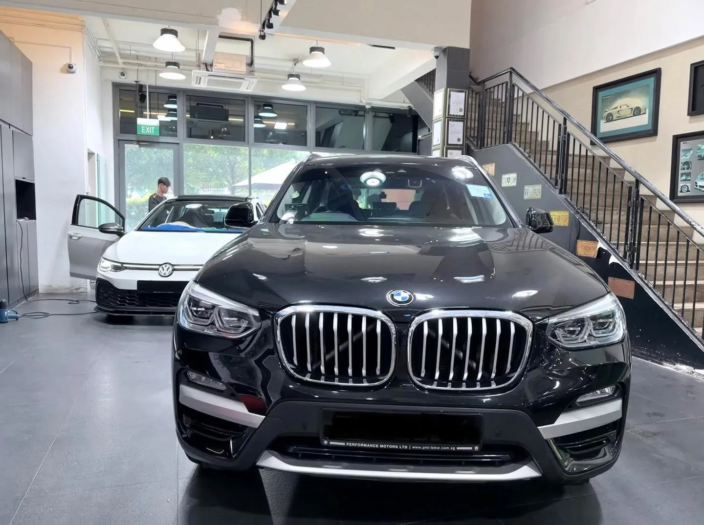 A white Volkswagen Golf hatchback and a black BMW X3 SUV inside the workshop.