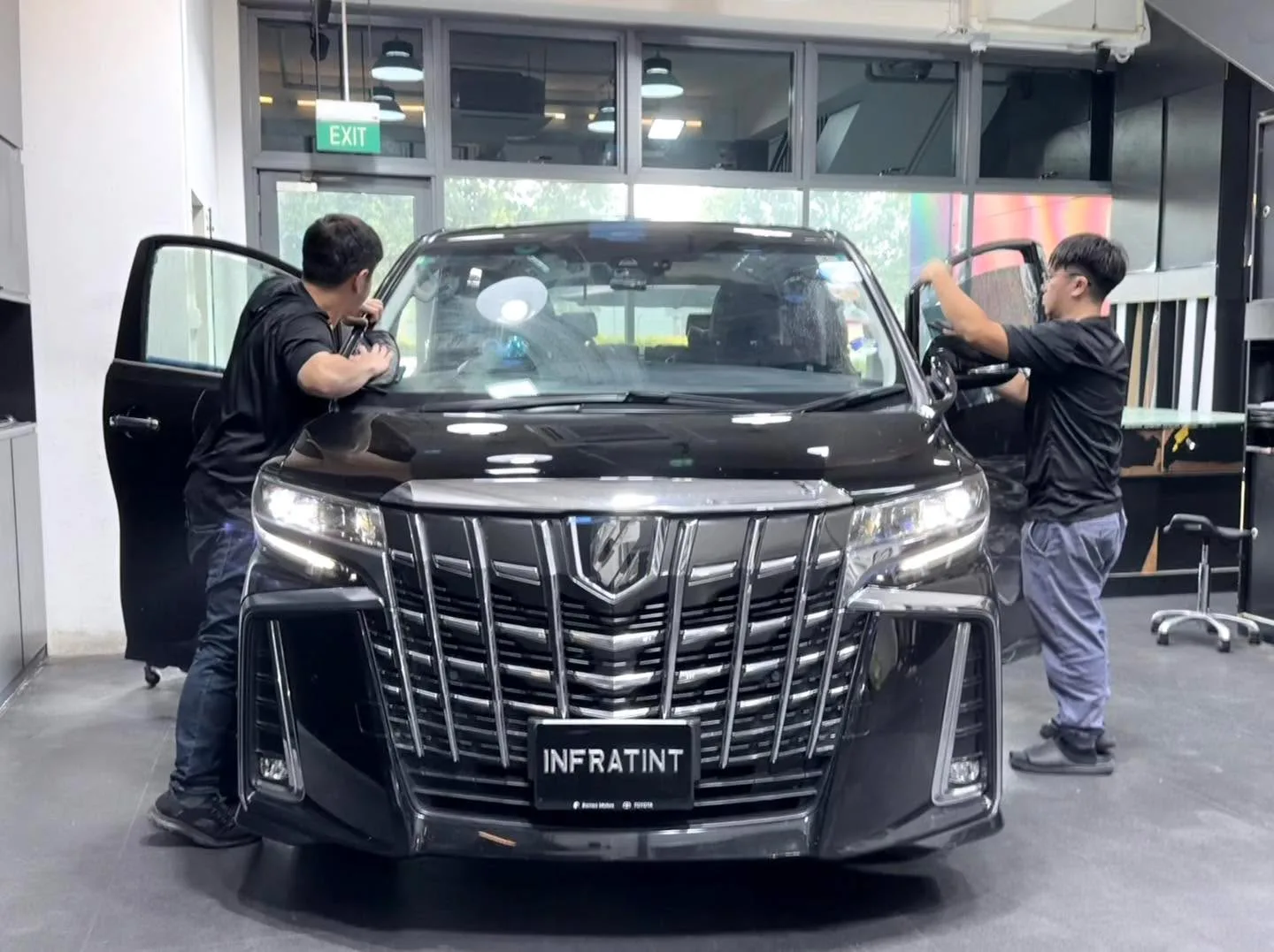 A black Toyota Alphard MPV with doors open and technicians working on windows.