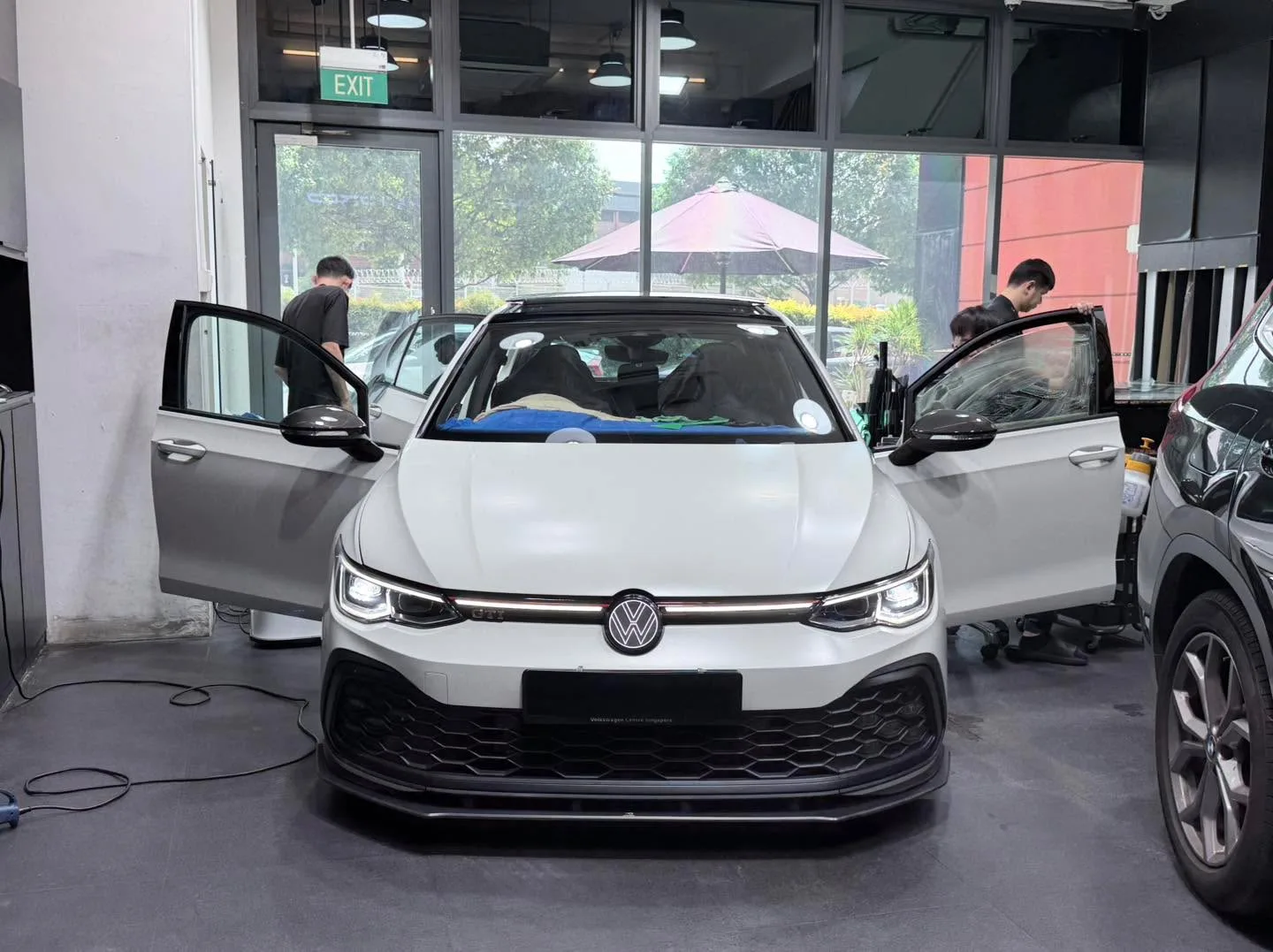 A white Volkswagen Golf hatchback with doors open and technician applying film.