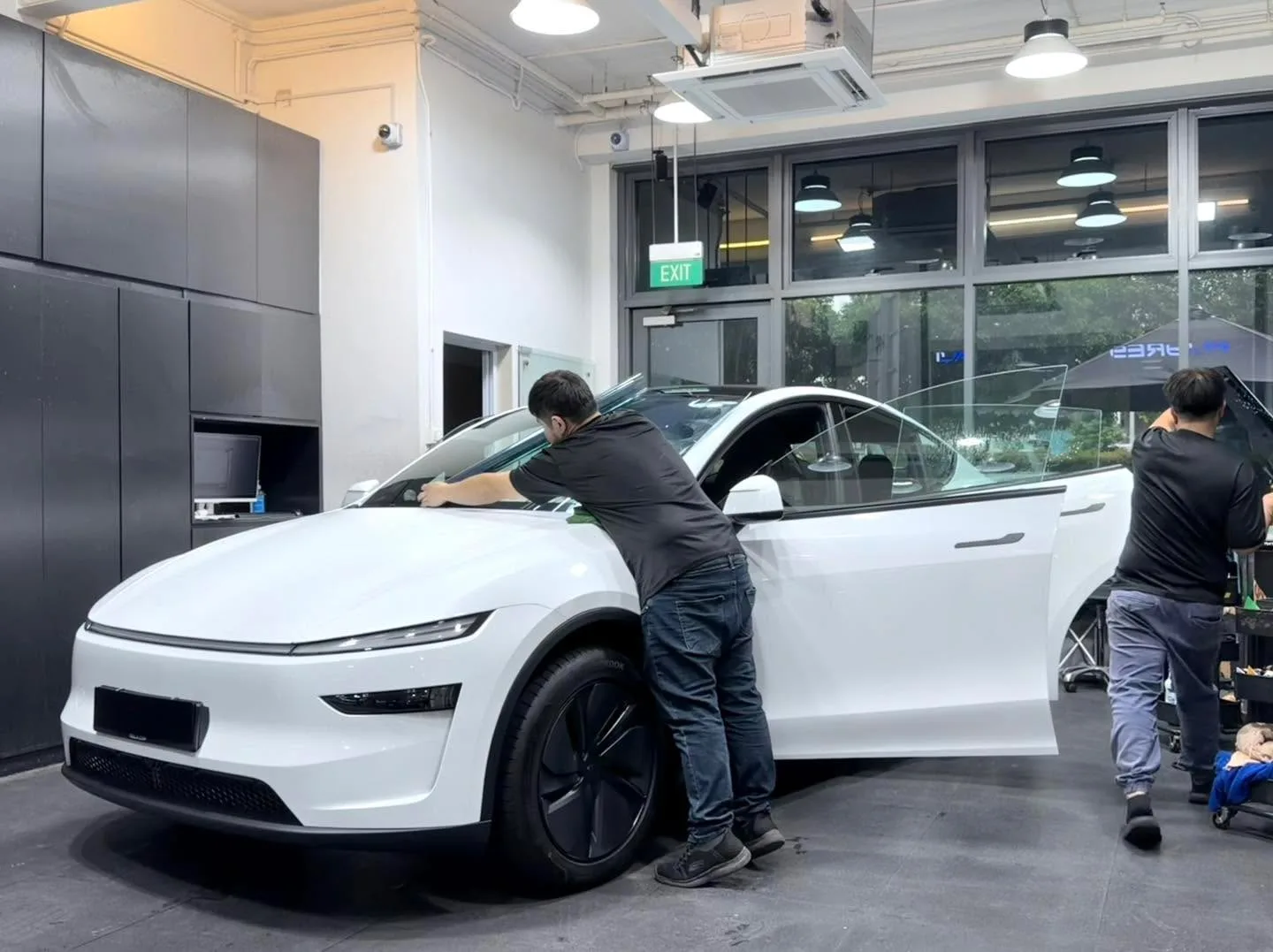A white Tesla Model Y with technicians applying tint film to the windows.