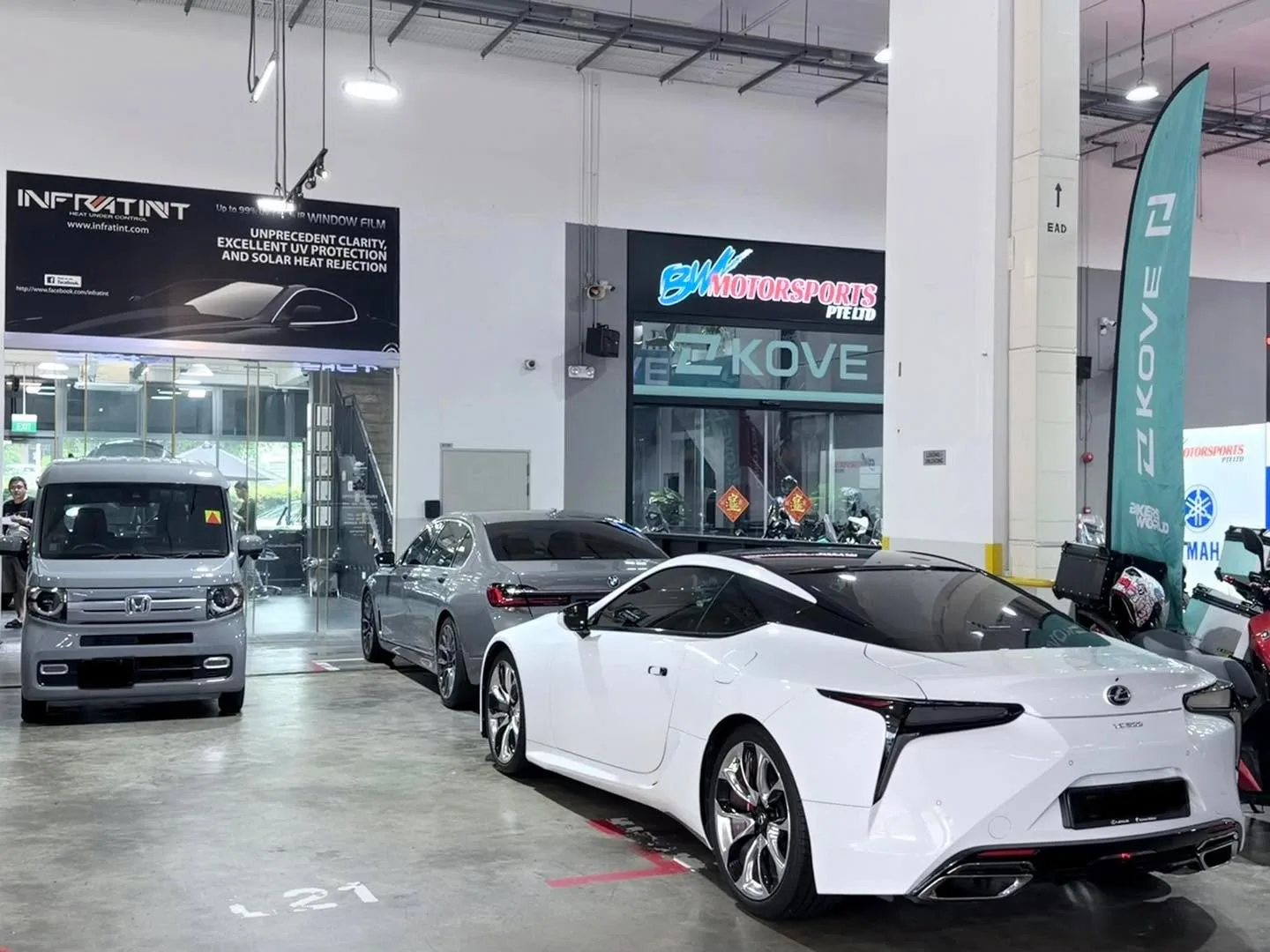 A white sports car and a silver saloon in an indoor workshop space.