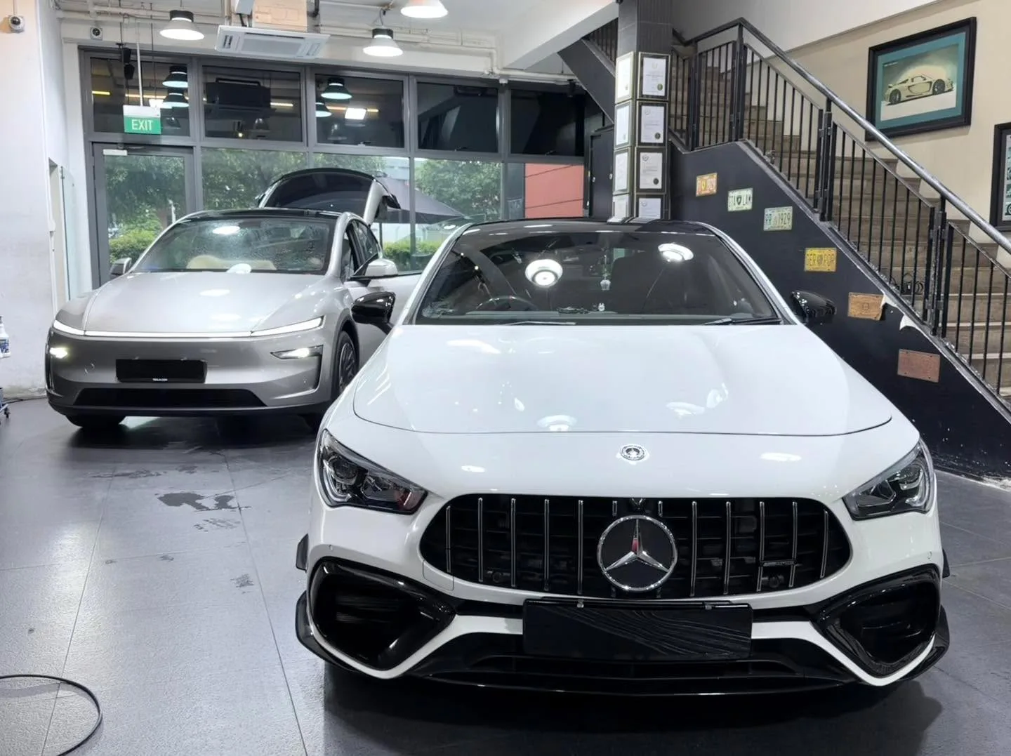 A white performance sedan with prominent grille and a silver electric saloon in a workshop.