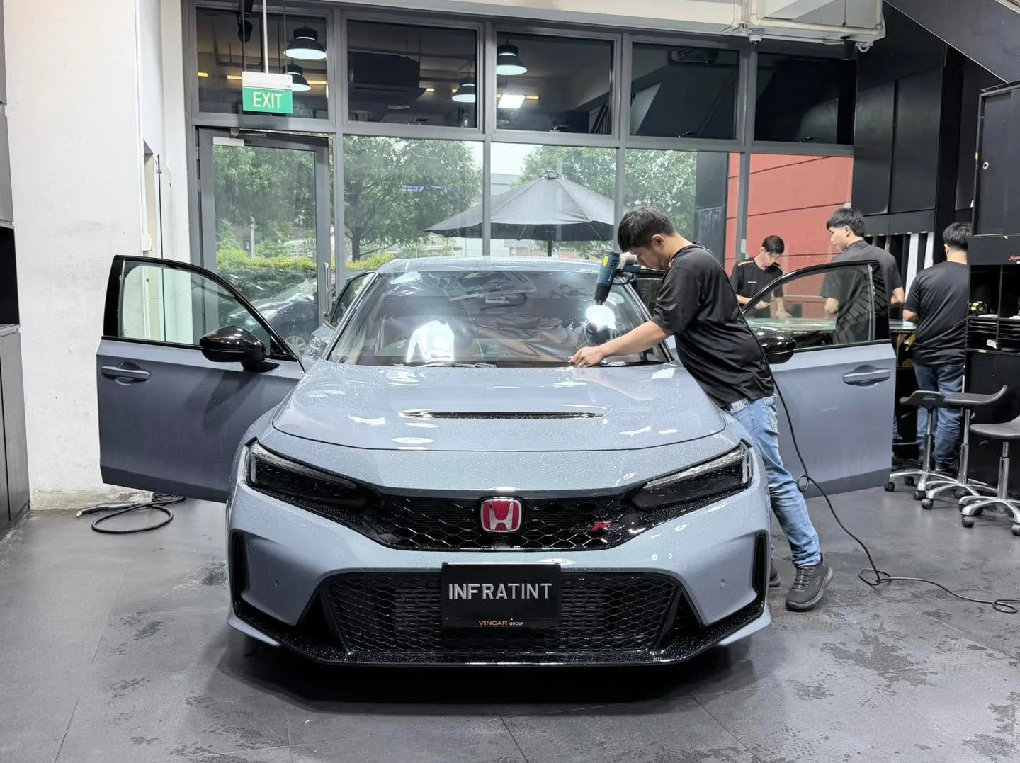 A silver hatchback with workers applying window tint to the front doors.