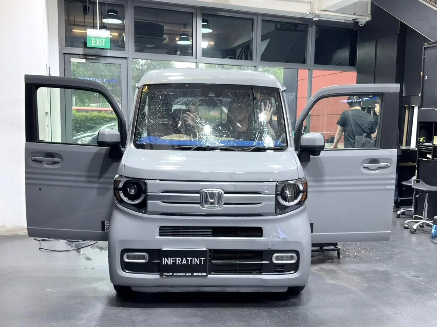A silver mini kei vehicle with its doors open, workers applying tint inside.
