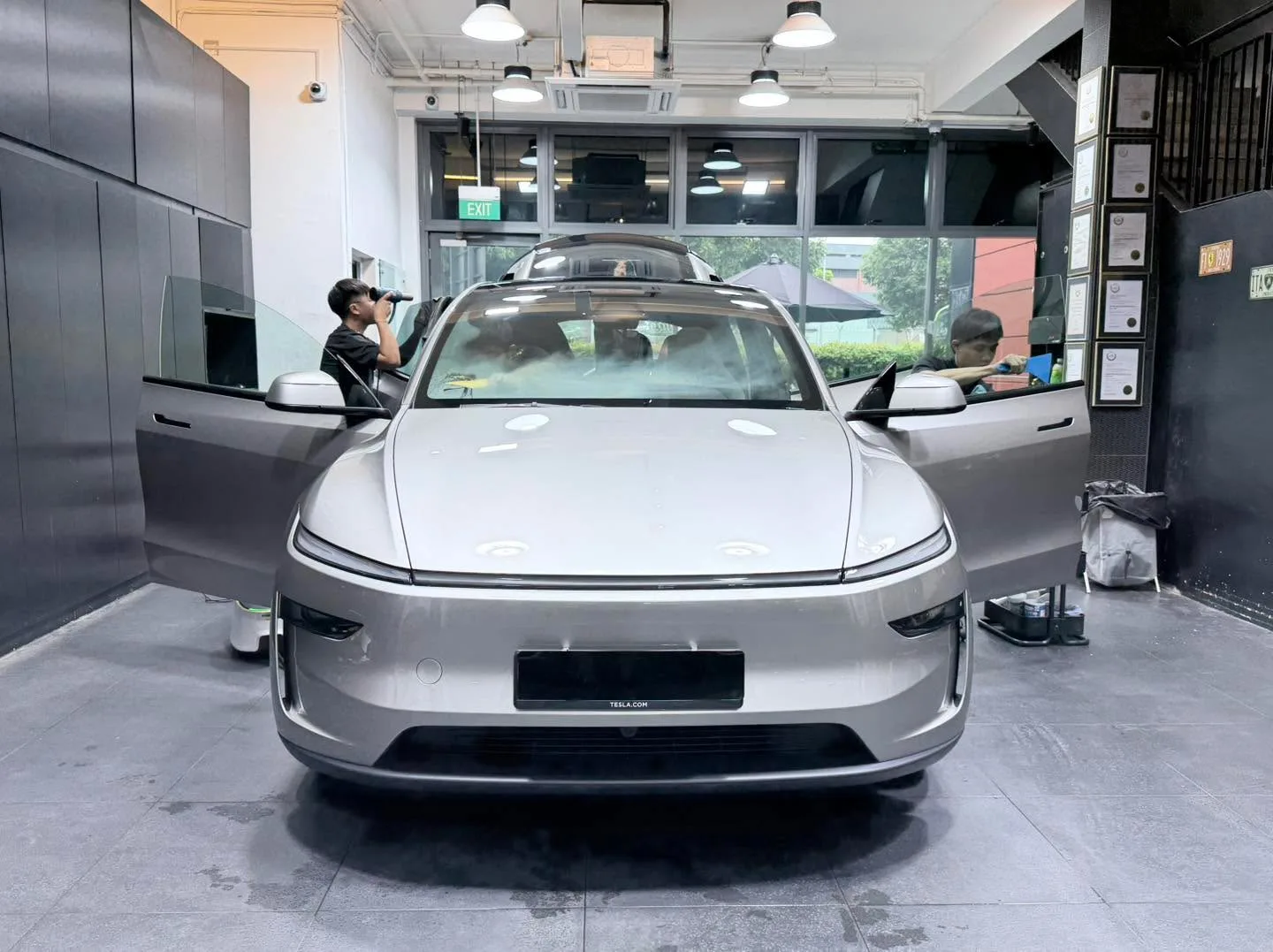 A silver electric sedan parked in the workshop, viewed from the front.