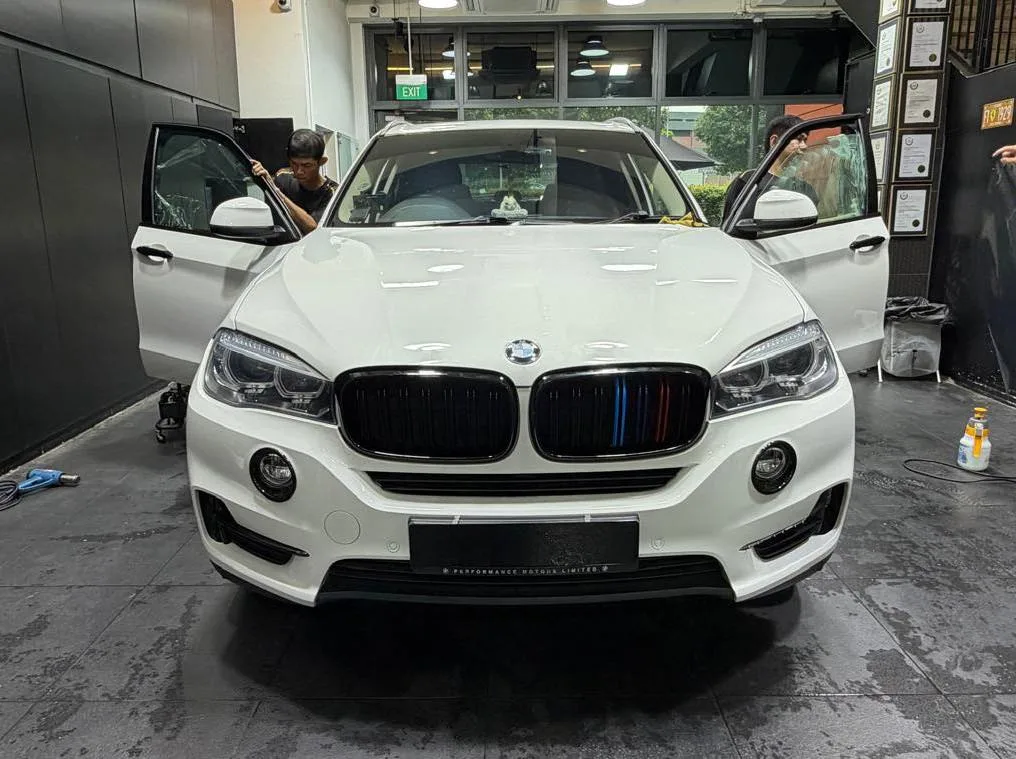A white SUV parked indoors with a worker applying tint to the side window.