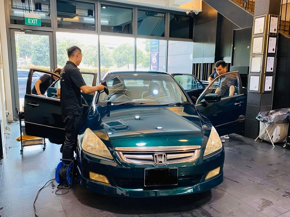 Two installers applying tint film to a dark green Honda Accord inside the Infratint workshop
