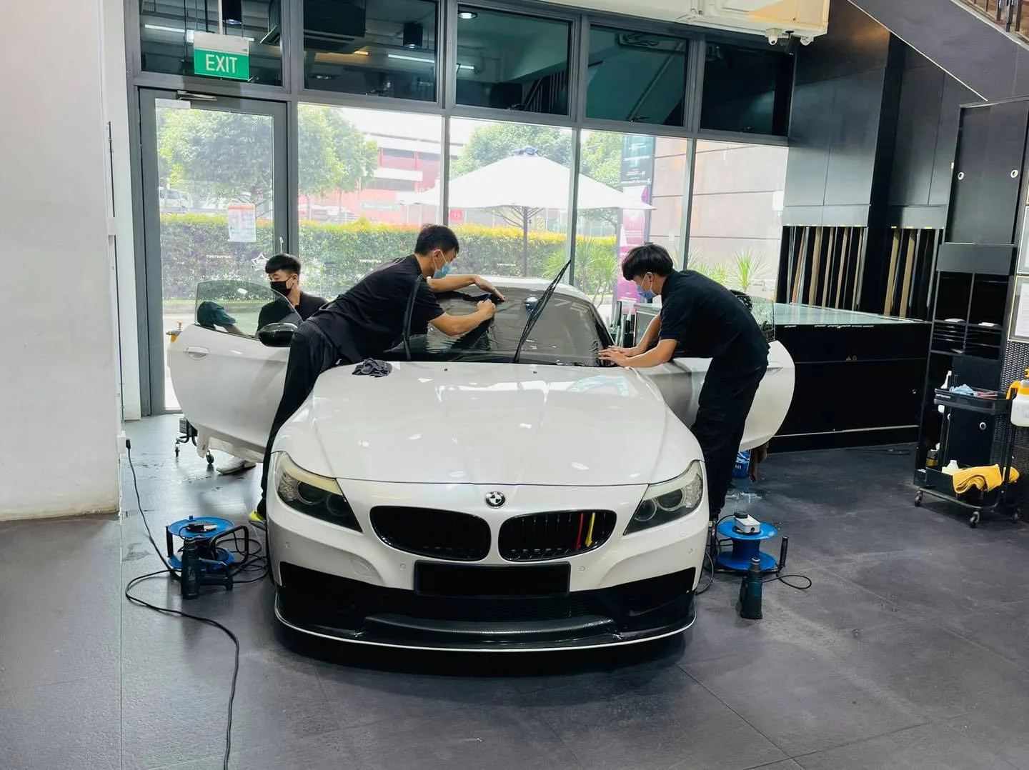 Three installers applying window film to a white BMW Z4 at Infratint Singapore