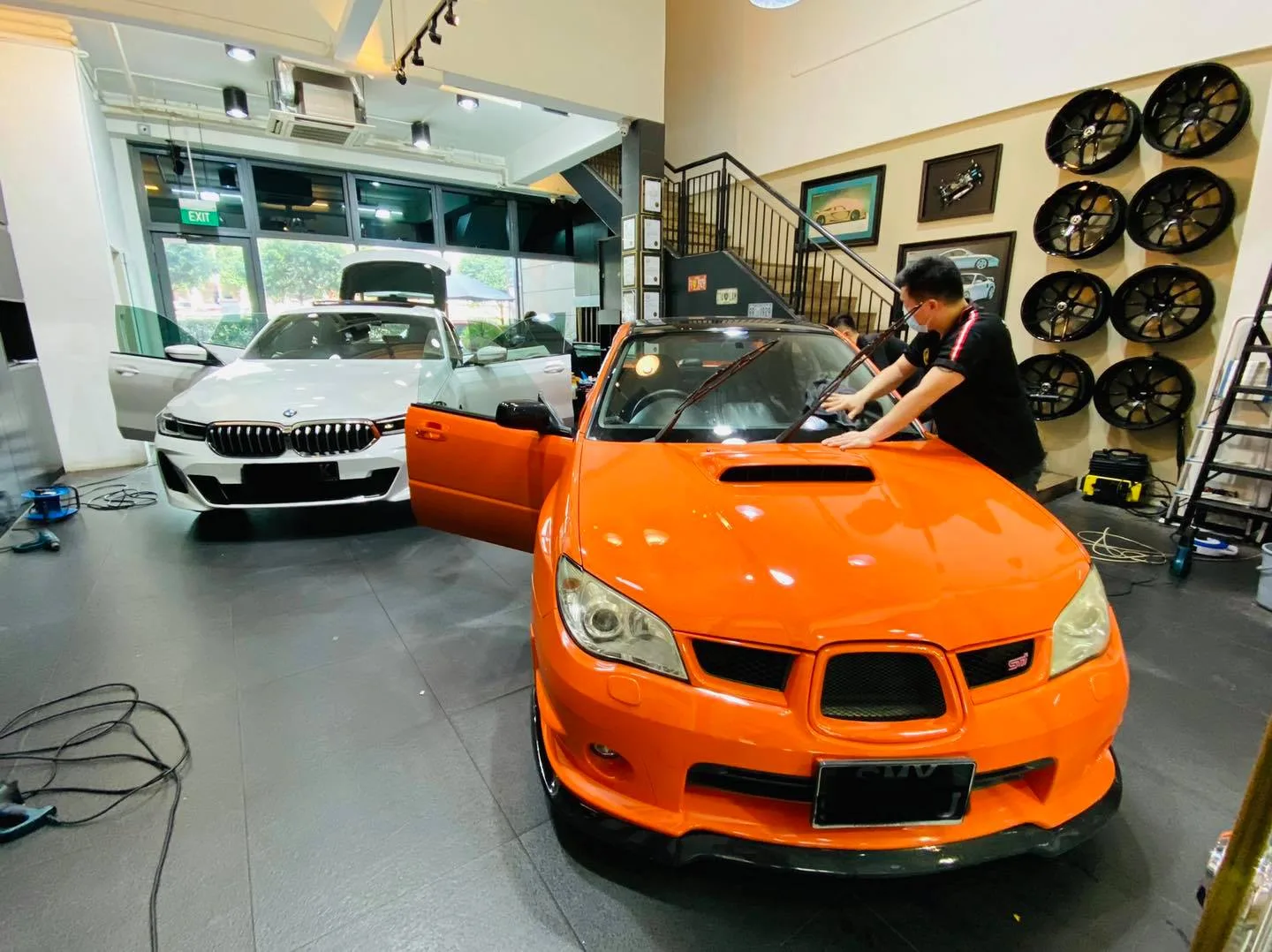Installer tinting an orange Subaru WRX next to a white BMW at Infratint Singapore