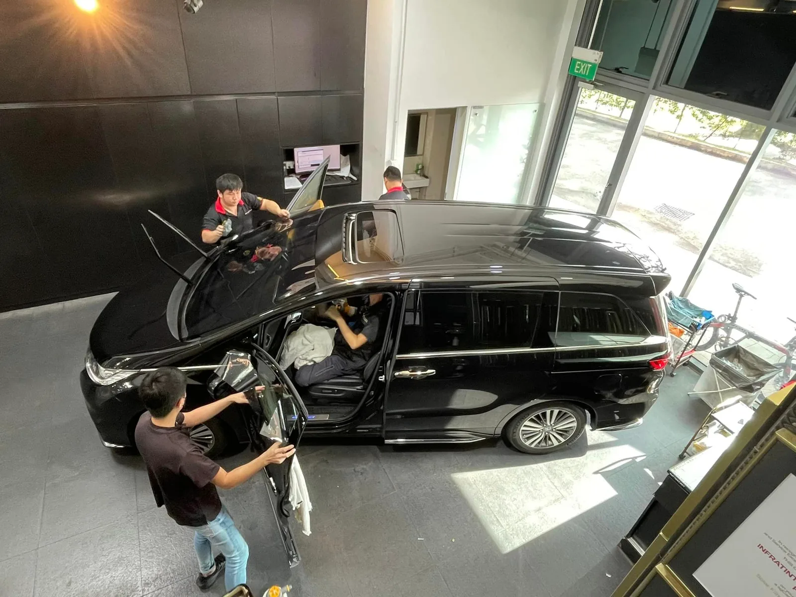 Overhead view of a black Honda Odyssey being tinted by three installers at Infratint Singapore