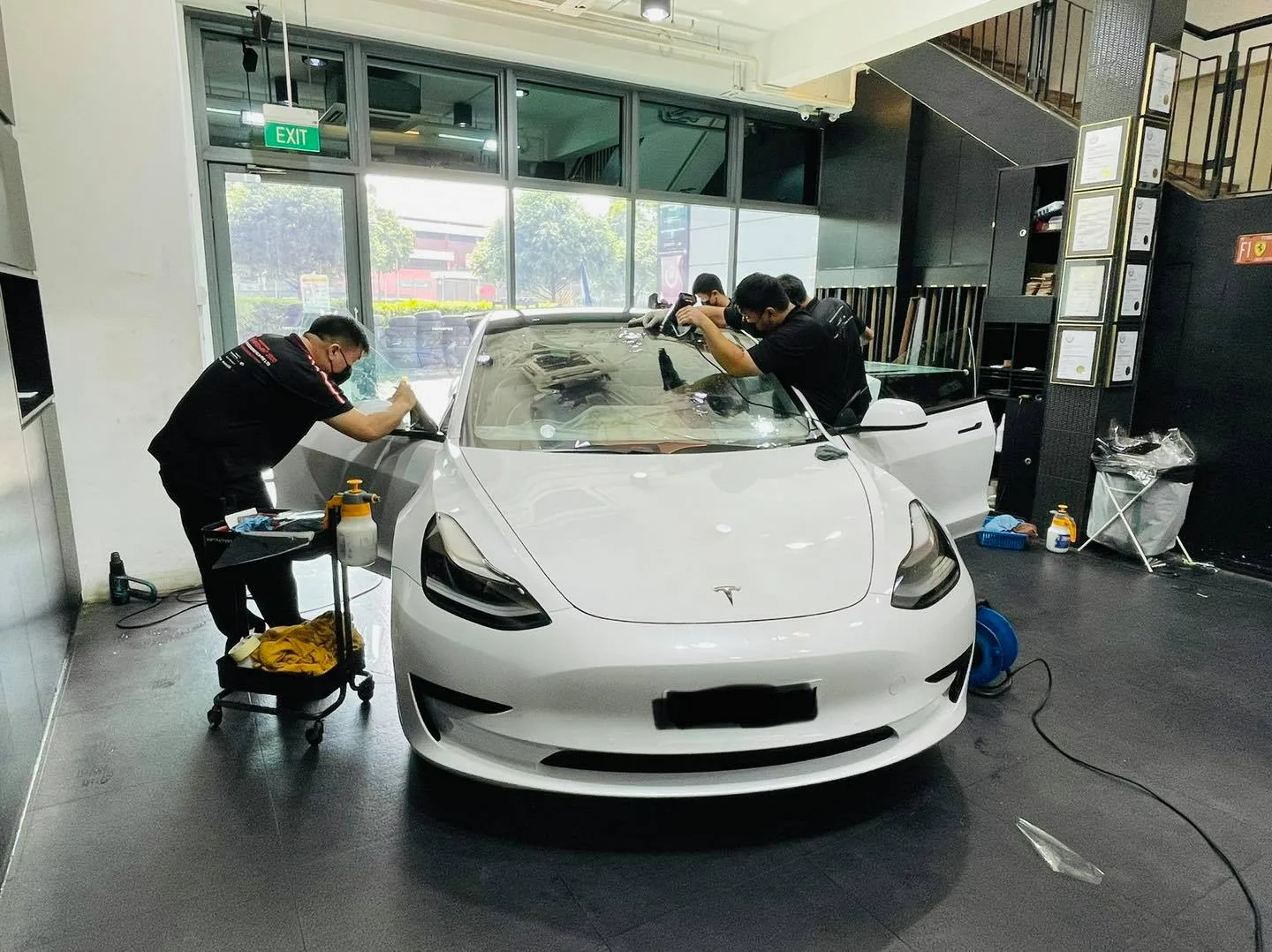 Installers applying window film to a white Tesla Model 3 at Infratint Singapore
