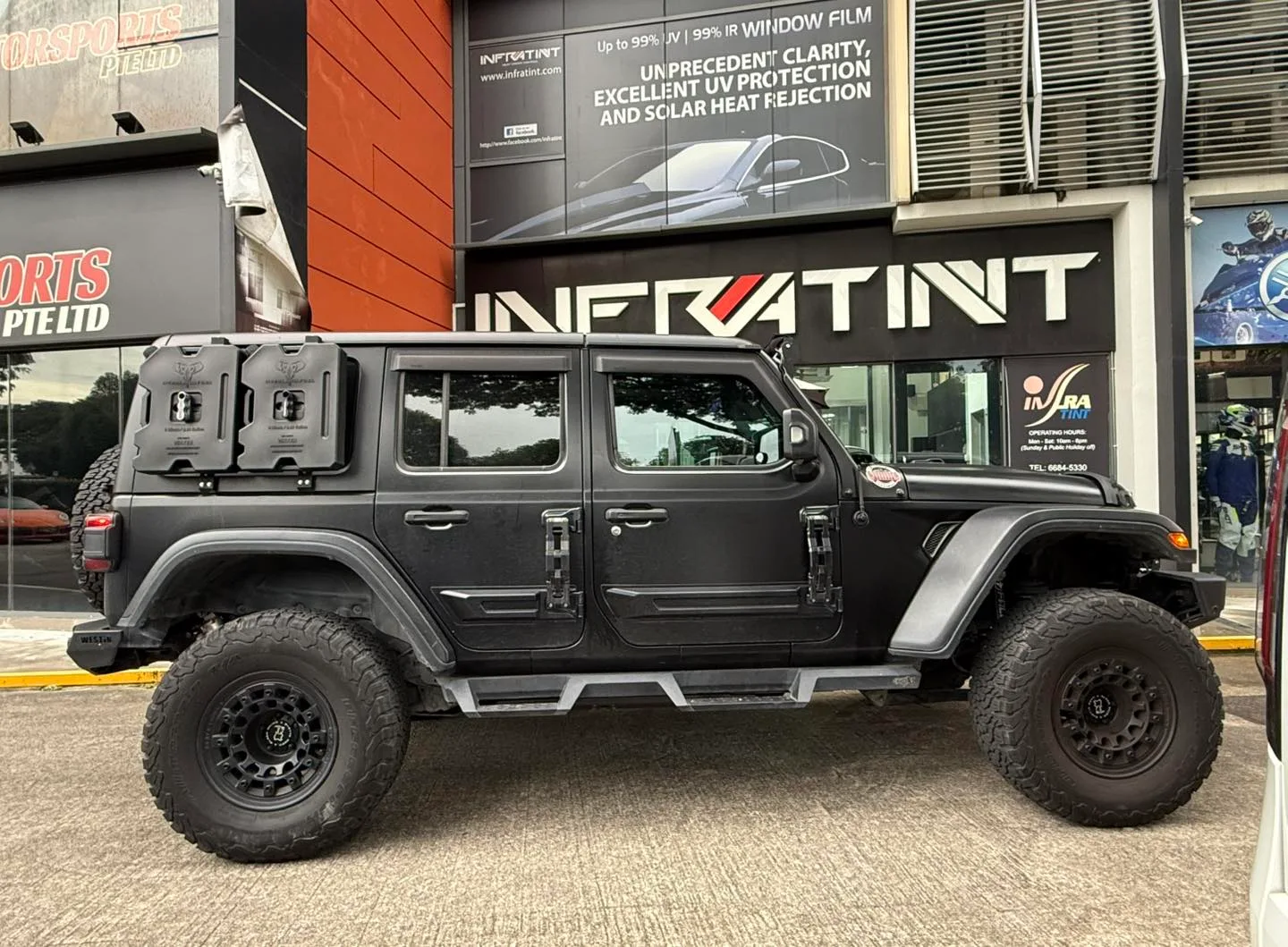 Dark grey Jeep Wrangler side profile outside Infratint Singapore signage