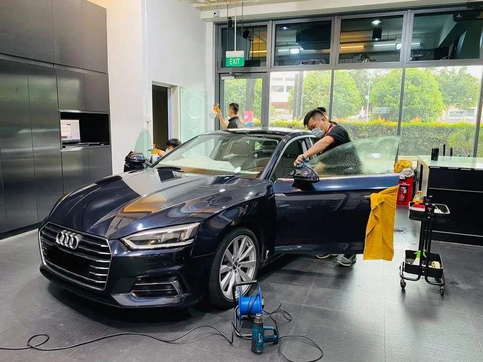 Installer squeegeeing film on a dark blue Audi sedan at Infratint Singapore