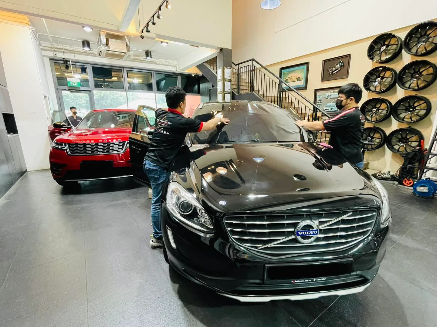 Technicians tinting a black Volvo XC60 with a red Range Rover behind at Infratint Singapore