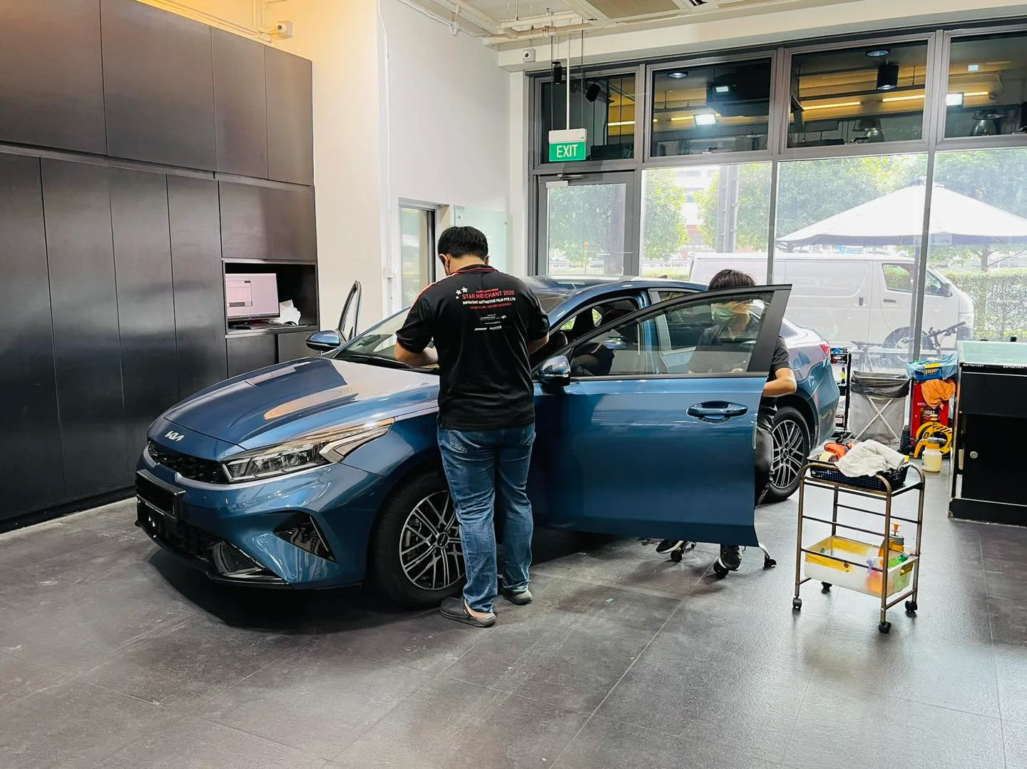 Technicians tinting the side windows of a blue Kia Cerato at Infratint Singapore
