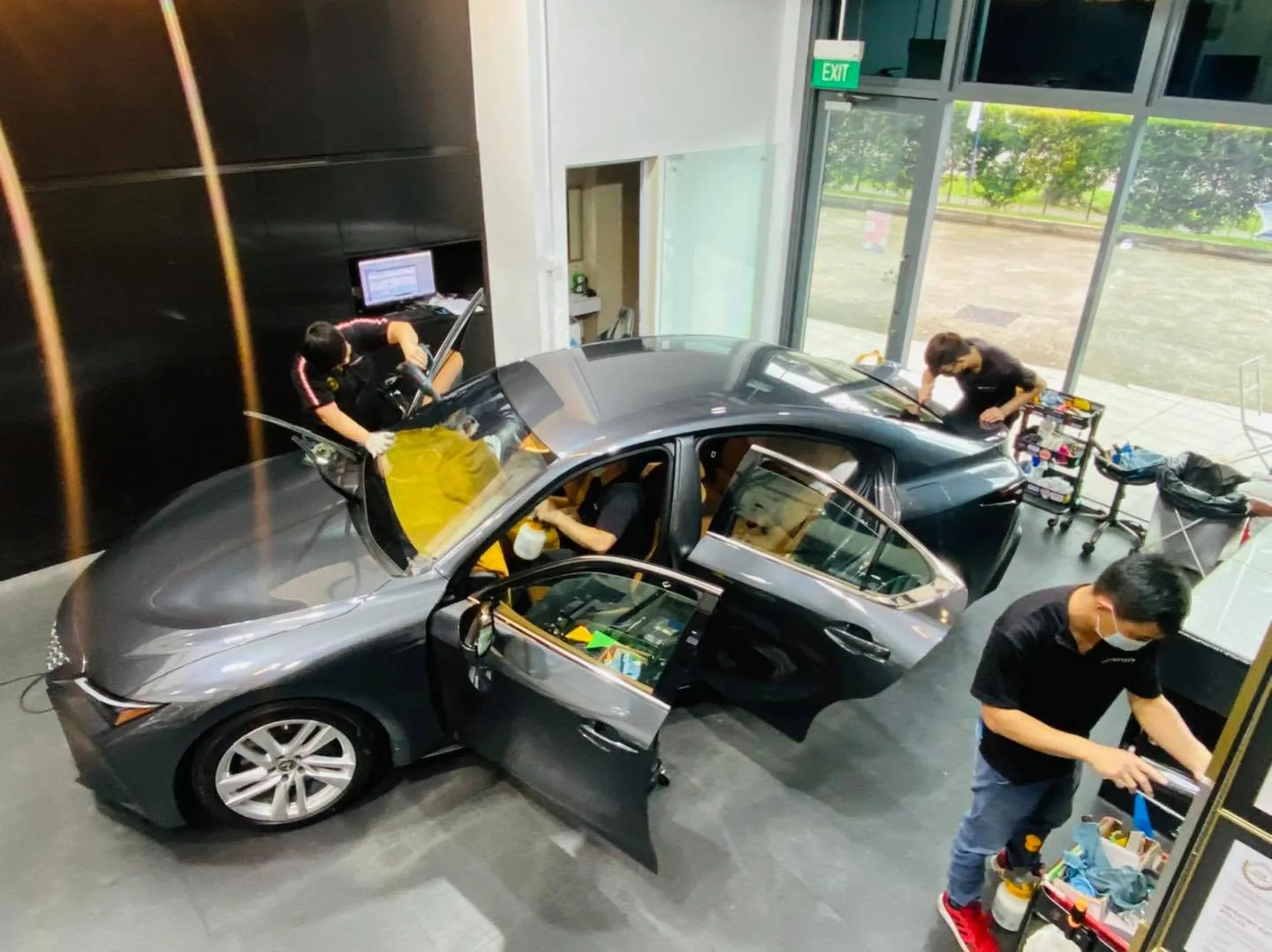 Overhead view of a grey Lexus sedan being tinted by three installers at Infratint Singapore