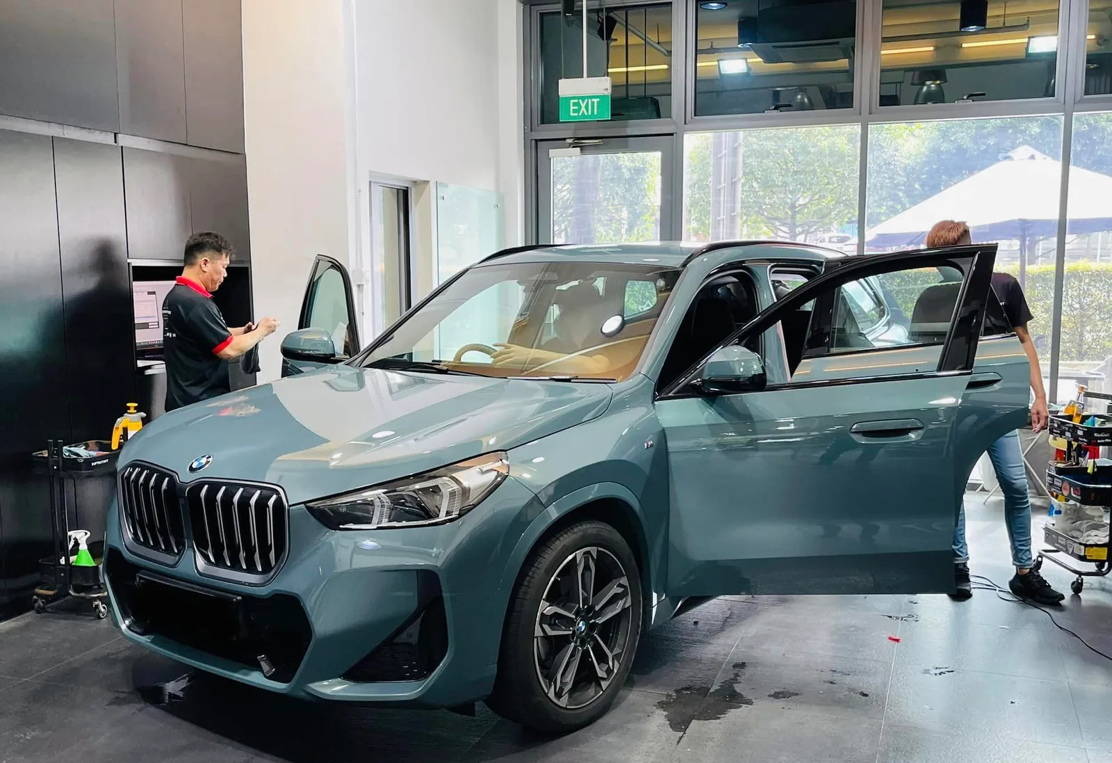 Teal BMW X1 SUV being window tinted by technicians at Infratint Singapore