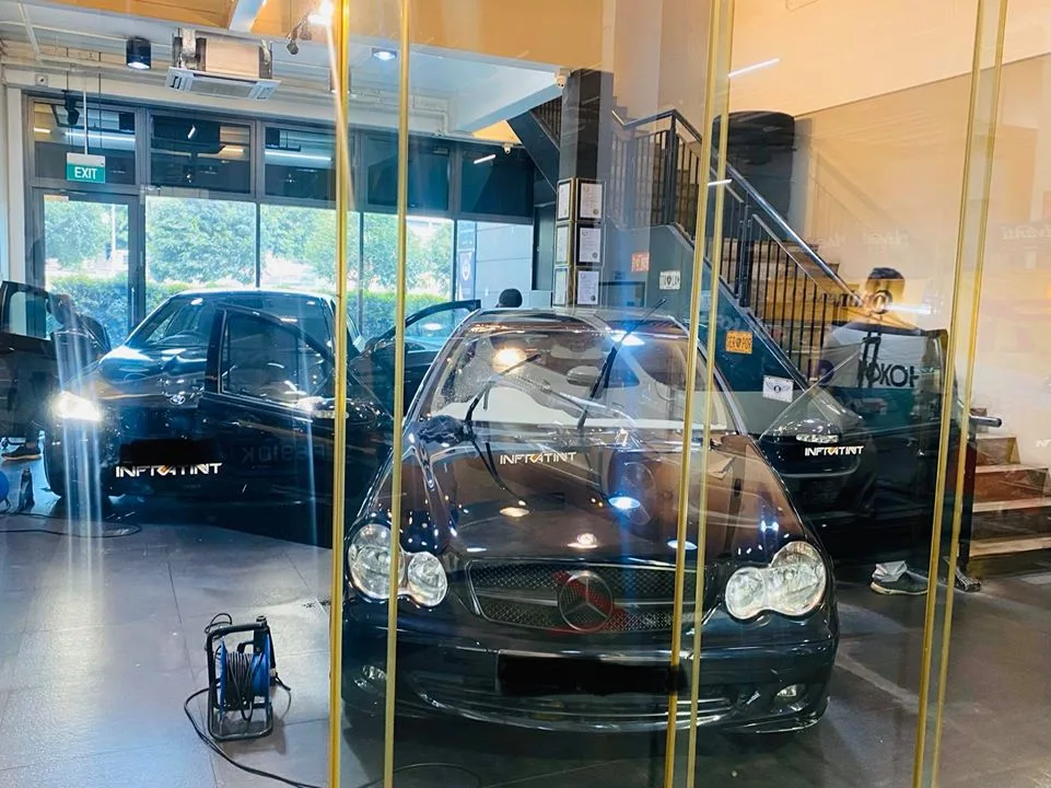 Black Mercedes-Benz C-Class sedan viewed through the showroom glass partition at Infratint Singapore