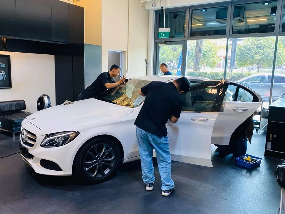 Installers fitting window film to a white Mercedes-Benz C-Class at Infratint Singapore
