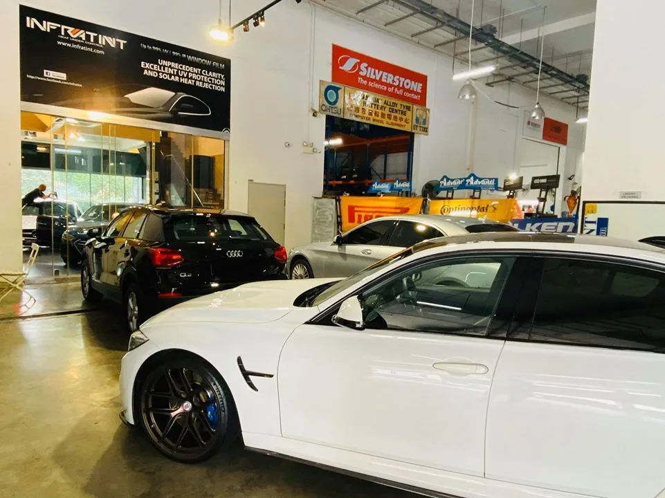 White BMW M3 sedan with blue brake calipers beside a black Audi Q2 at Infratint Singapore