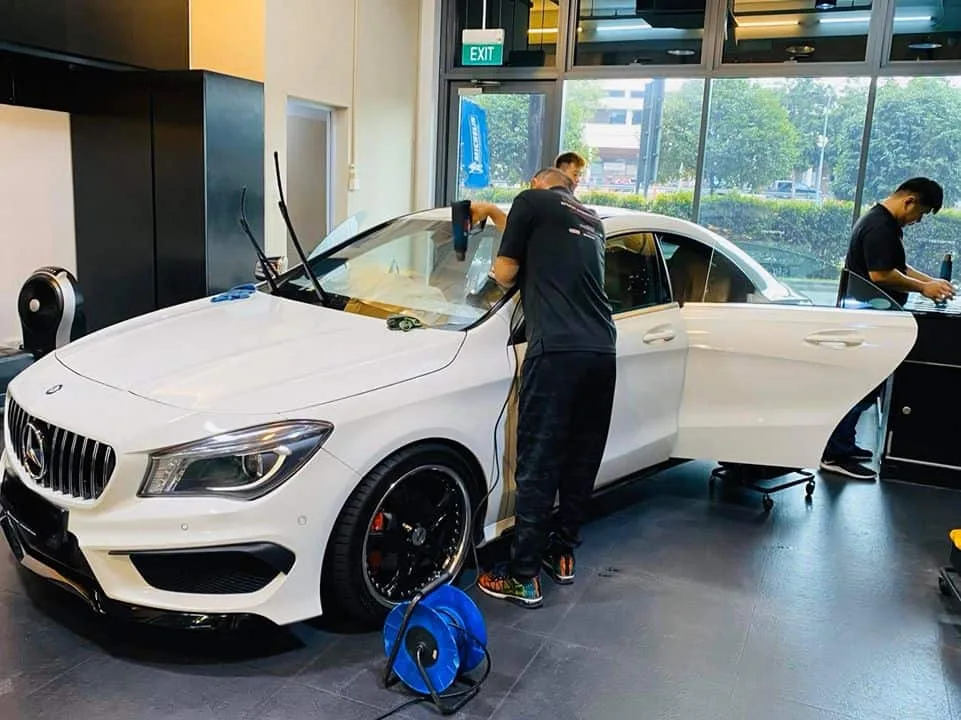 Technician using a heat gun on a white Mercedes-Benz CLA during window film installation at Infratint Singapore