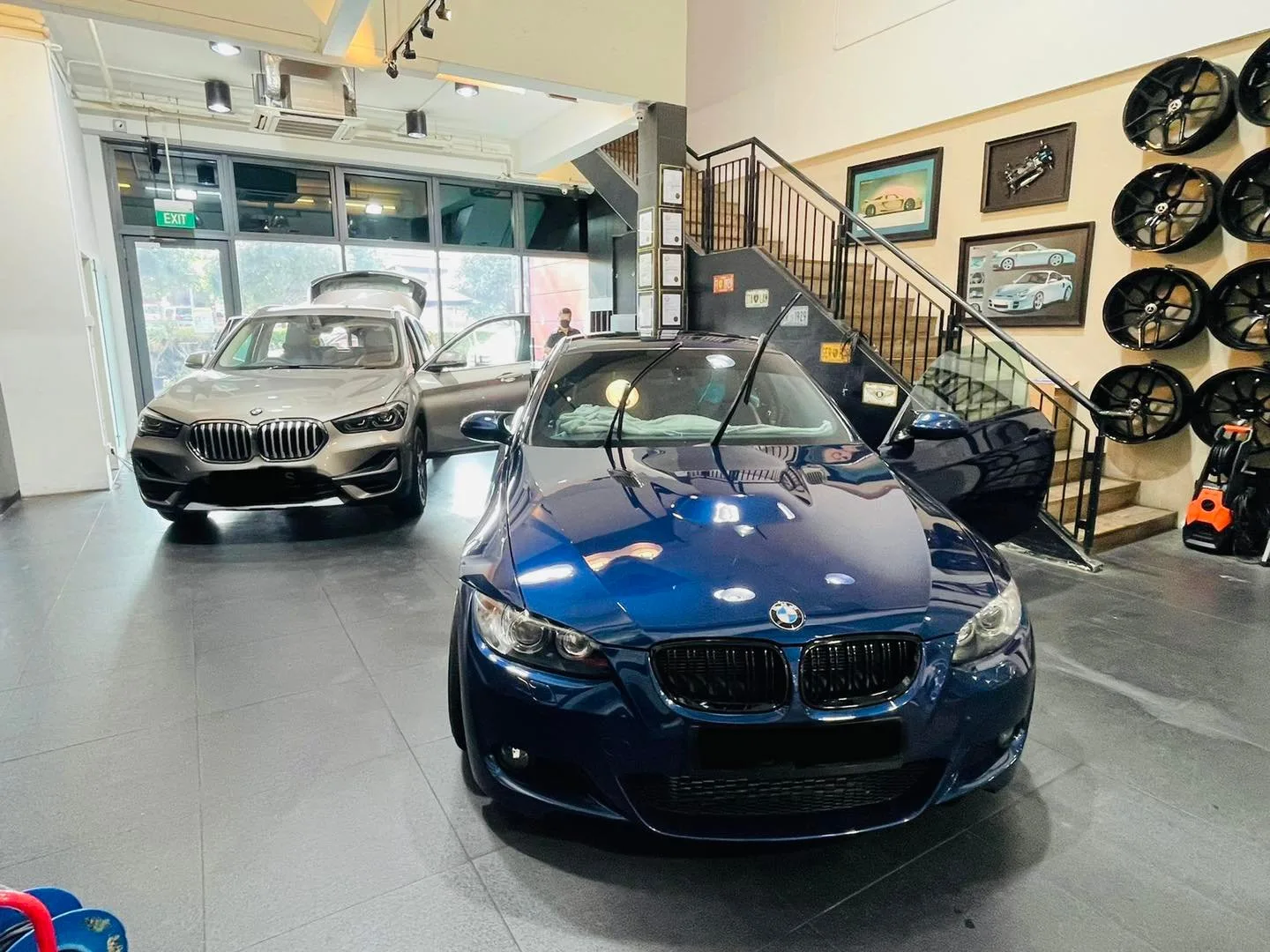 Blue BMW coupe and grey BMW SUV beside the wheel display at Infratint Singapore