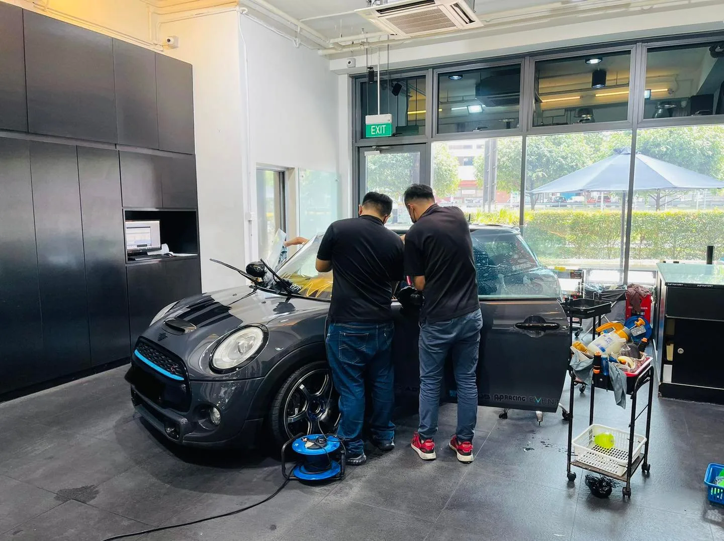 Two installers applying window film to a black Mini Cooper at Infratint Singapore