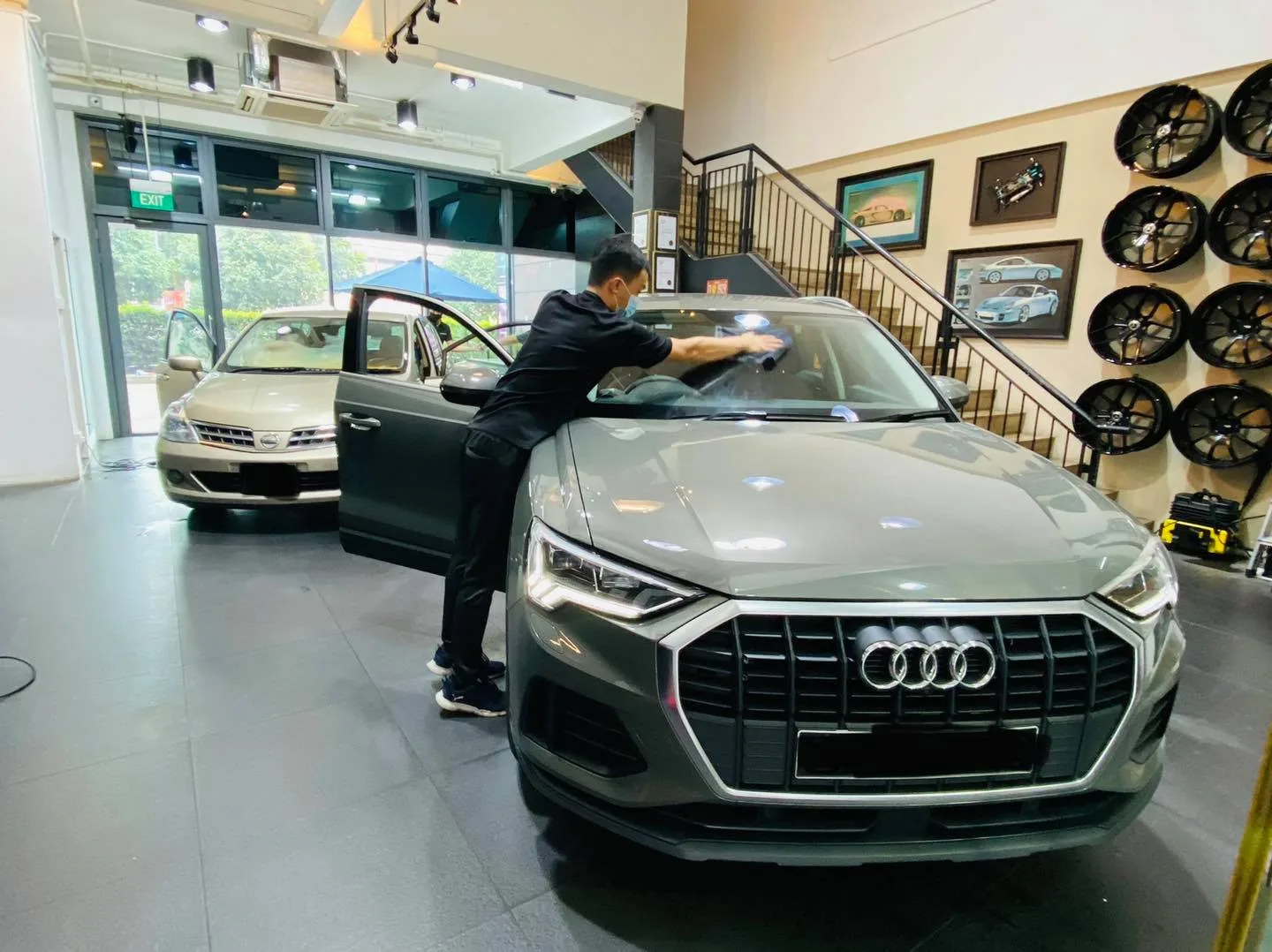 Grey Audi SUV being cleaned during window tinting beside a gold Nissan Latio at Infratint Singapore