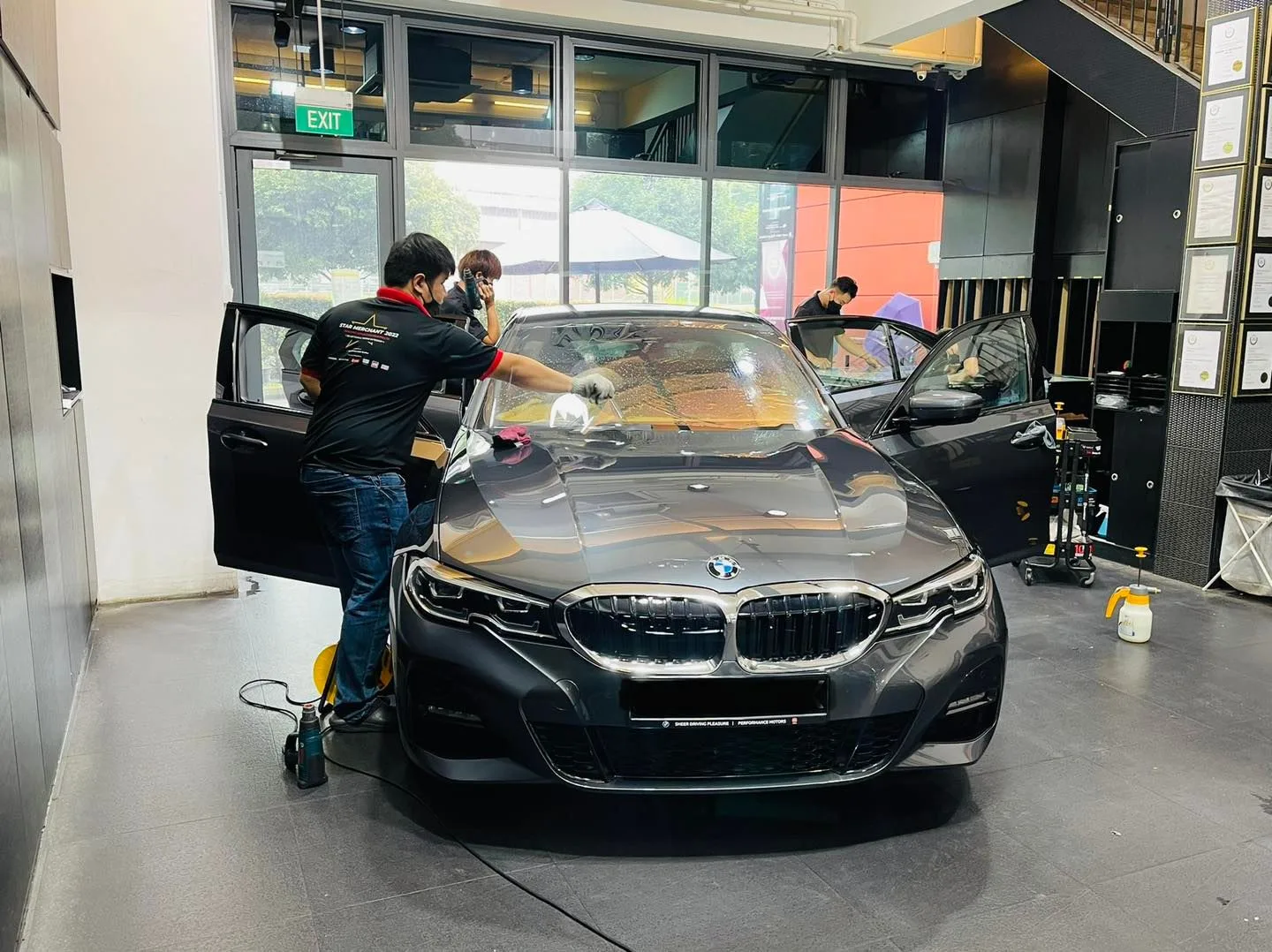 Technician applying window film to a grey BMW 3 Series windscreen at Infratint Singapore