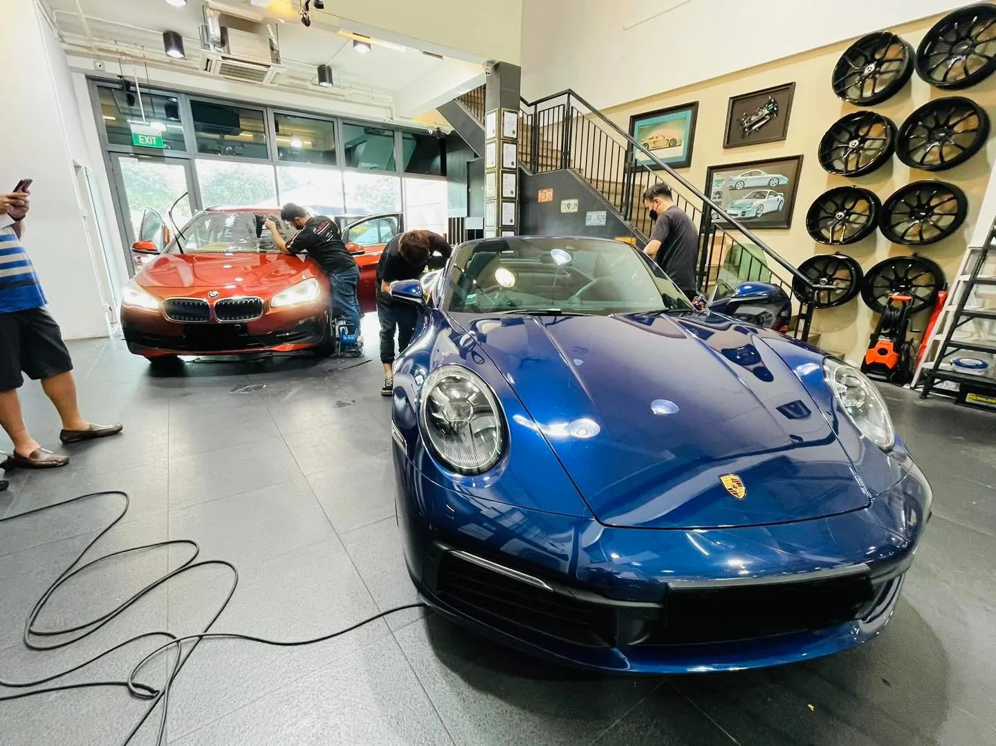 Blue Porsche 911 Carrera and orange BMW beside the alloy wheel wall at Infratint Singapore