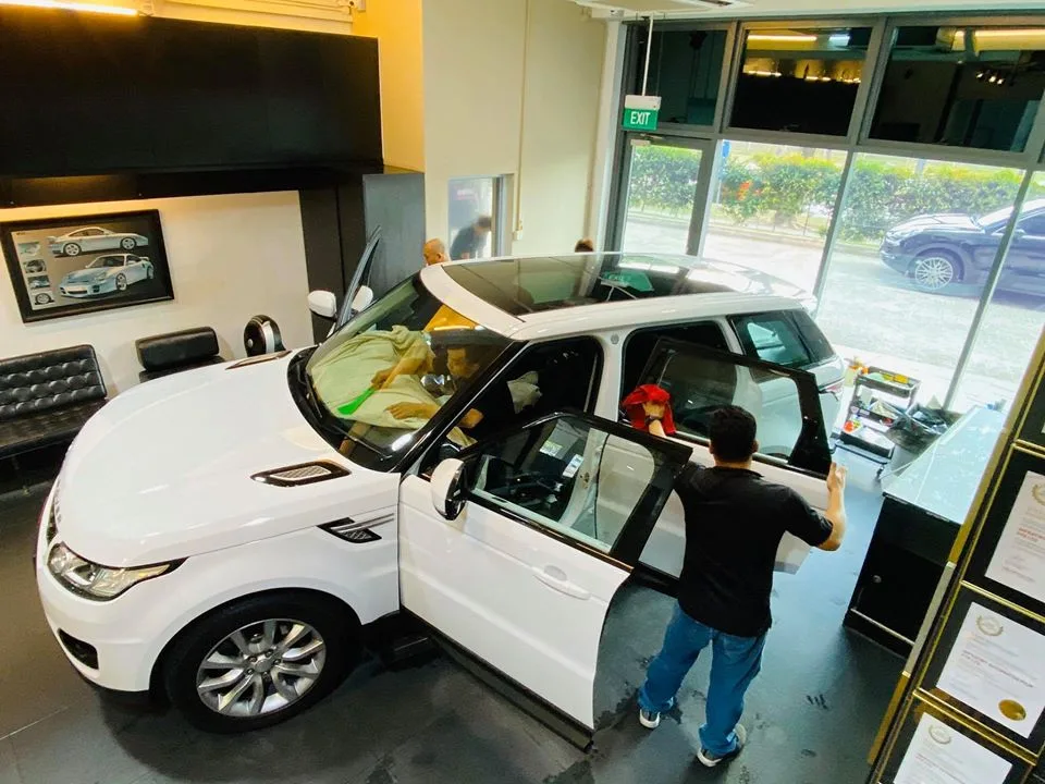 Technician tinting the rear door of a white Range Rover Sport at Infratint Singapore