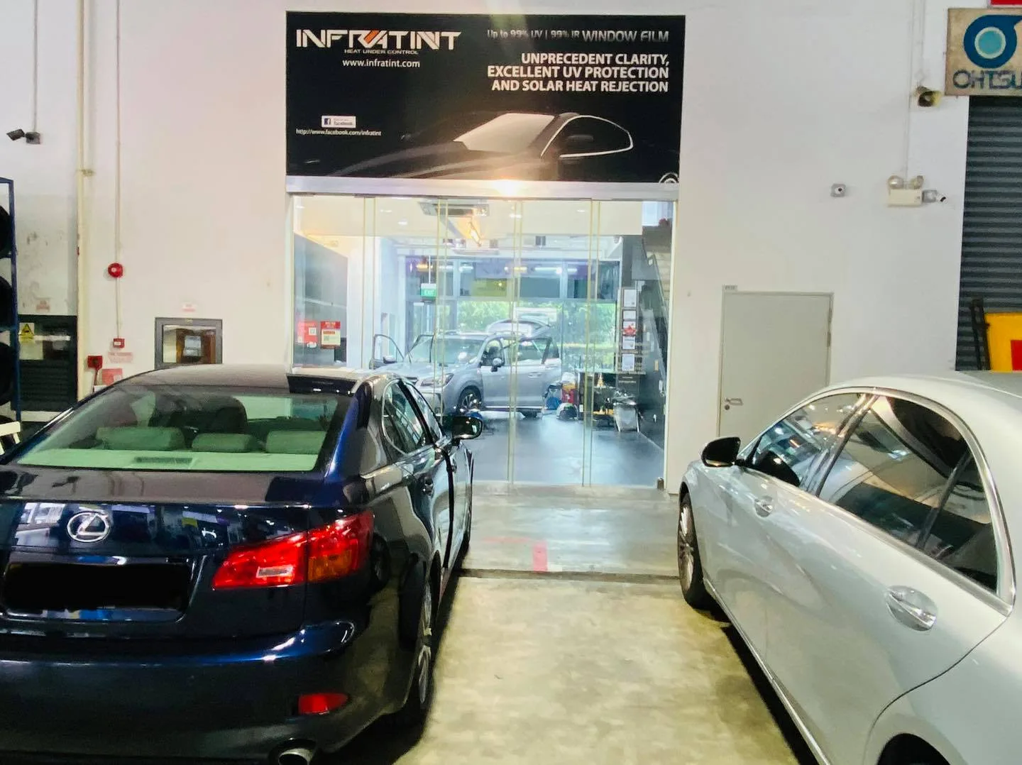 Dark blue Lexus IS and silver sedan by the Infratint Singapore banner for window tinting