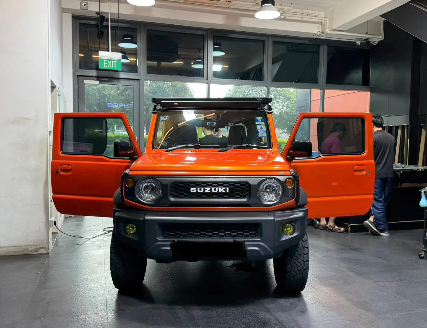 Orange Suzuki Jimny with doors open during tinting inside the Infratint workshop