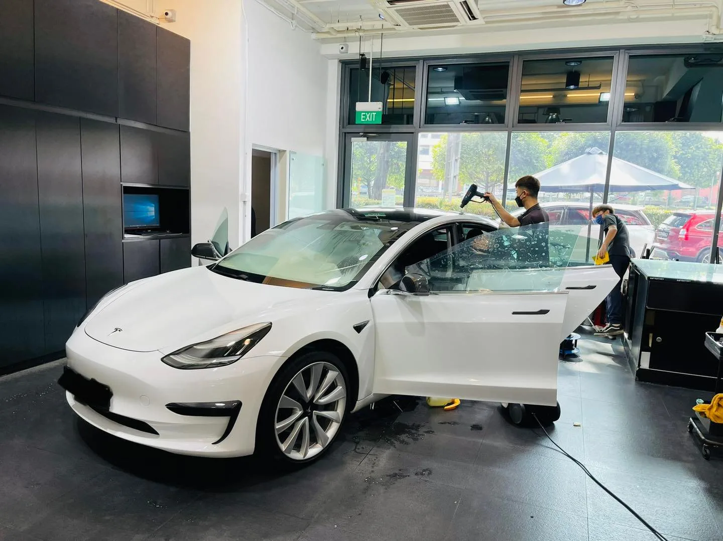 Technician tinting the windscreen of a white Tesla Model 3 at Infratint Singapore