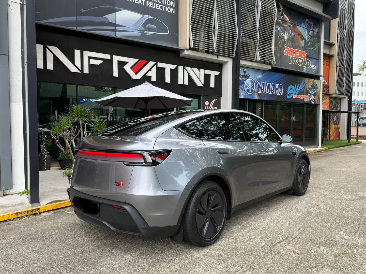 Silver Tesla Model Y Juniper rear three-quarter with tail light bar outside Infratint Singapore