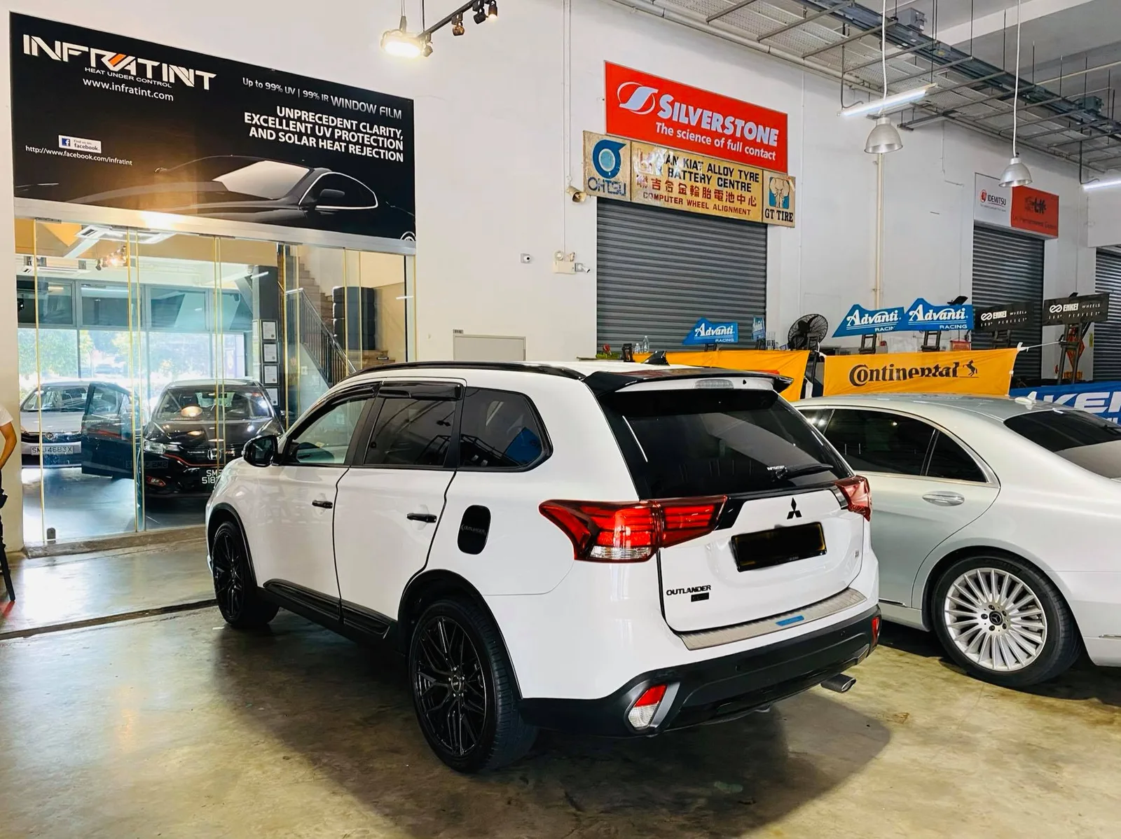 White Mitsubishi Outlander SUV rear view beside a silver Mercedes-Benz at Infratint Singapore