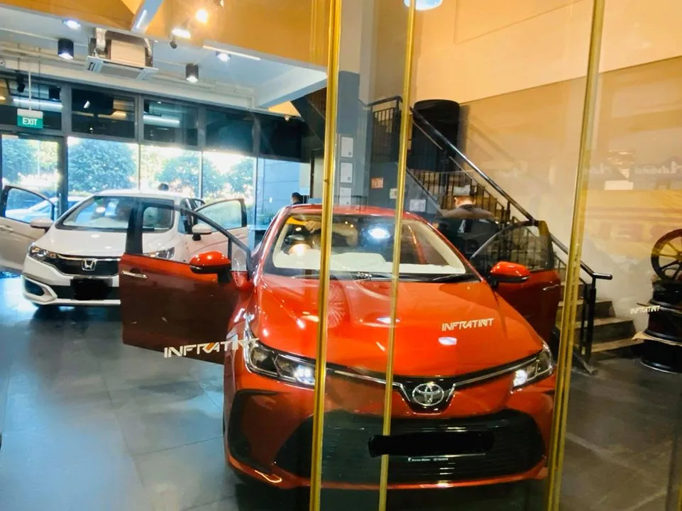 Orange Toyota Corolla sedan and white Honda viewed through Infratint Singapore showroom glass