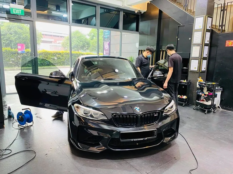 Black BMW M2 coupe being window tinted by two installers at Infratint Singapore